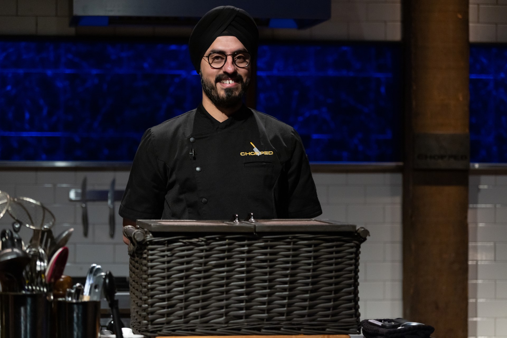 Jassi Bindra, dressed in all black, standing before a basket on an episode of “Chopped.”