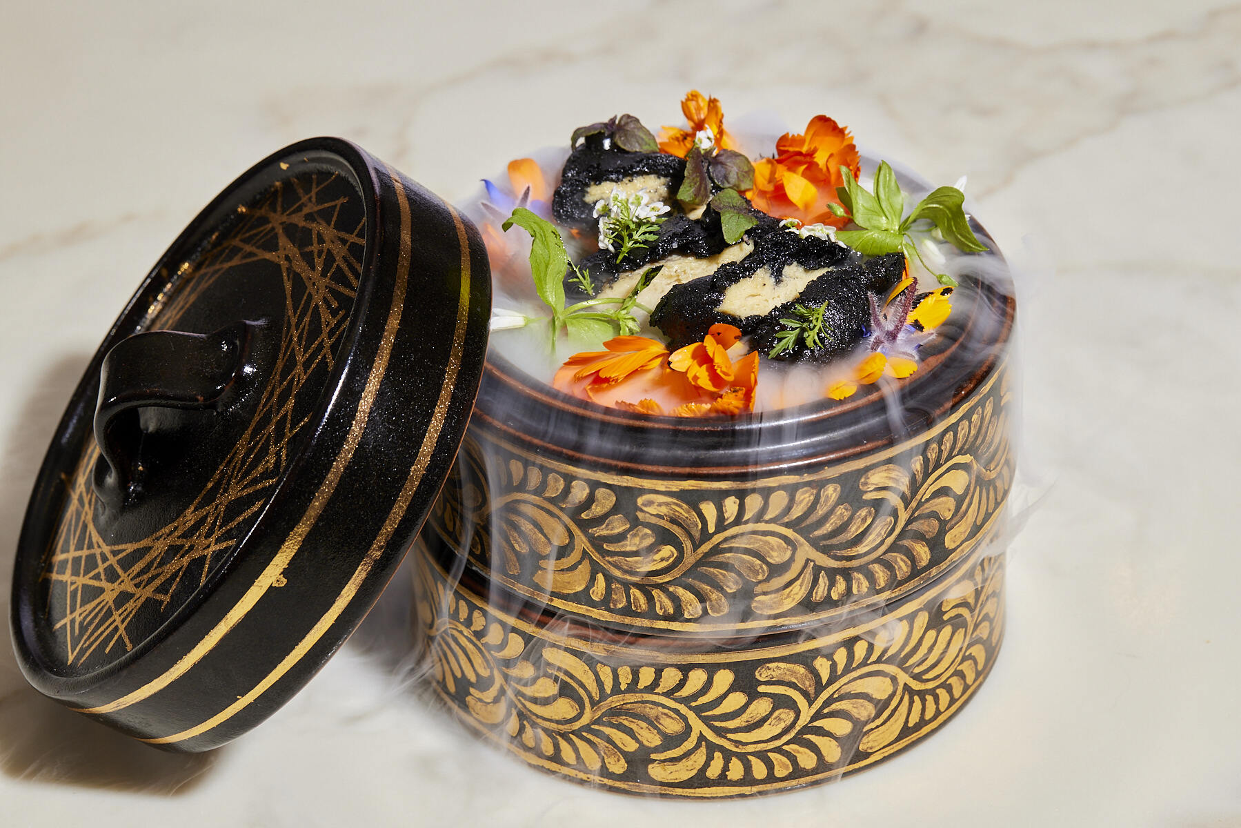 A round platter of food decorated with edible flowers and dry ice.
