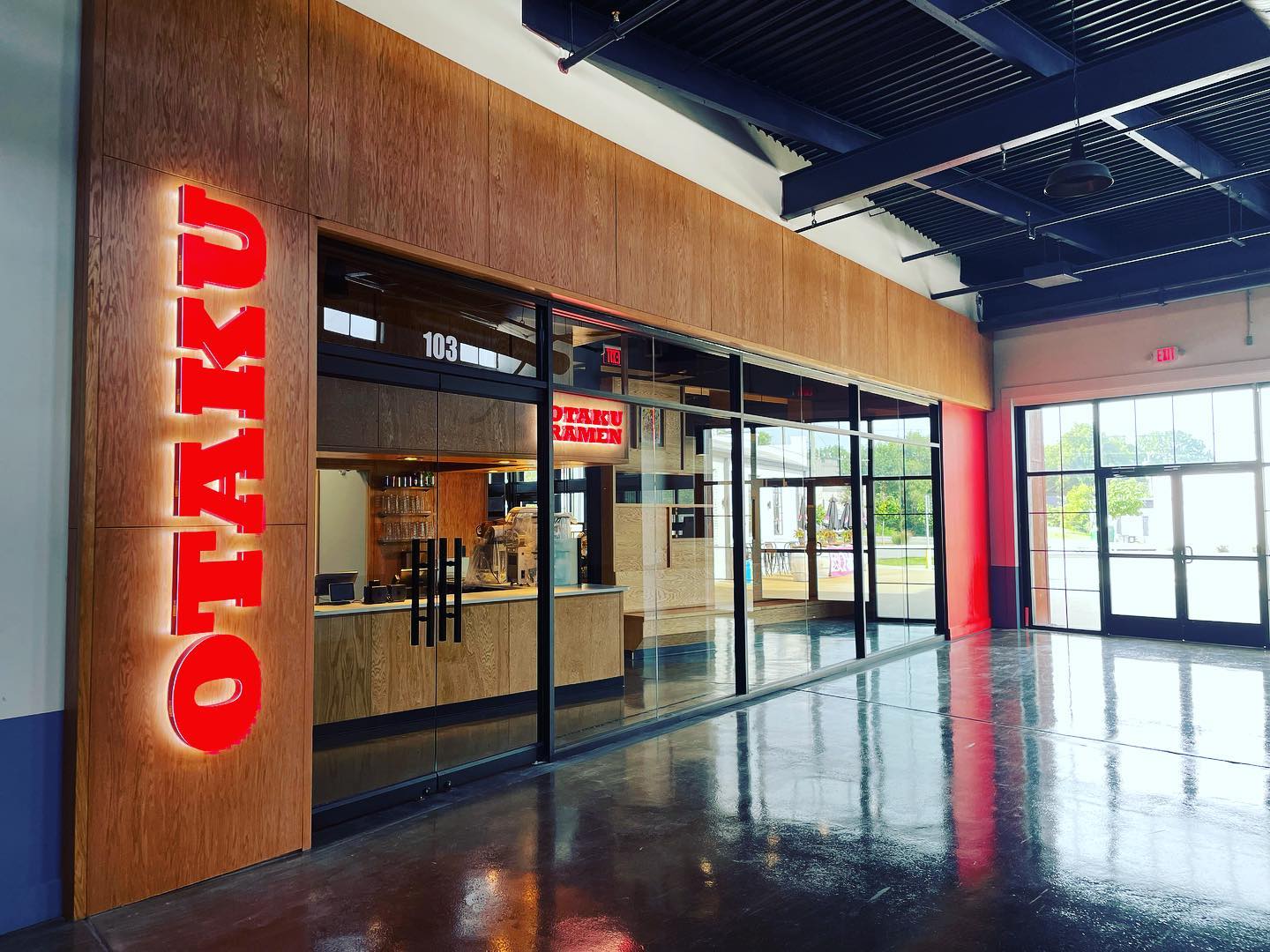 Indoor entrance to Otaku Ramen featuring a bright red sign that reads “Otaku” and polished glass doors and windows. 