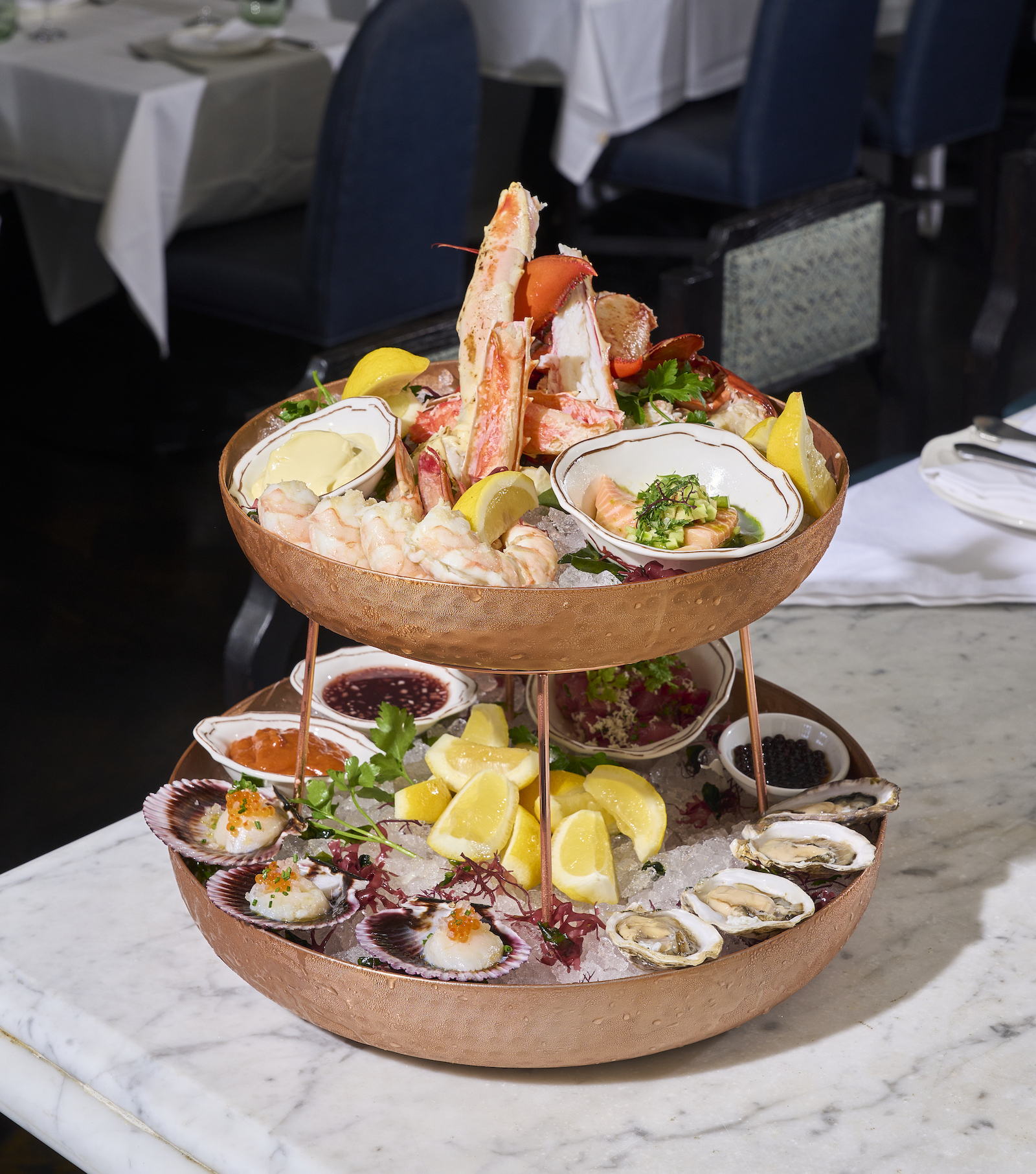 A bright look at a two-tiered seafood tower with shellfish and more on ice against a table at new restaurant Shirley Brasserie in Los Angeles.
