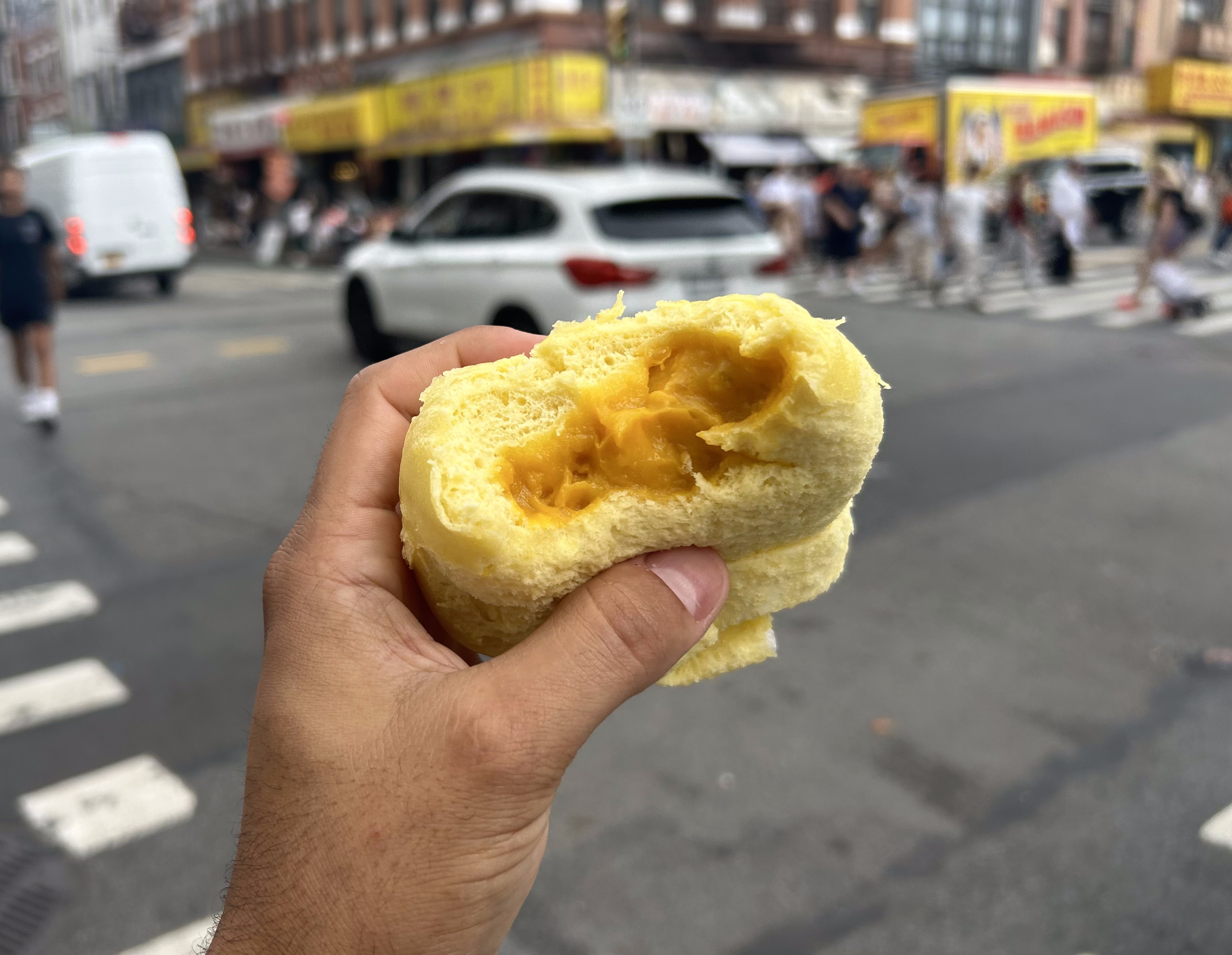 A hand holds a pumpkin bun with a bite out of it on a New York street corner.