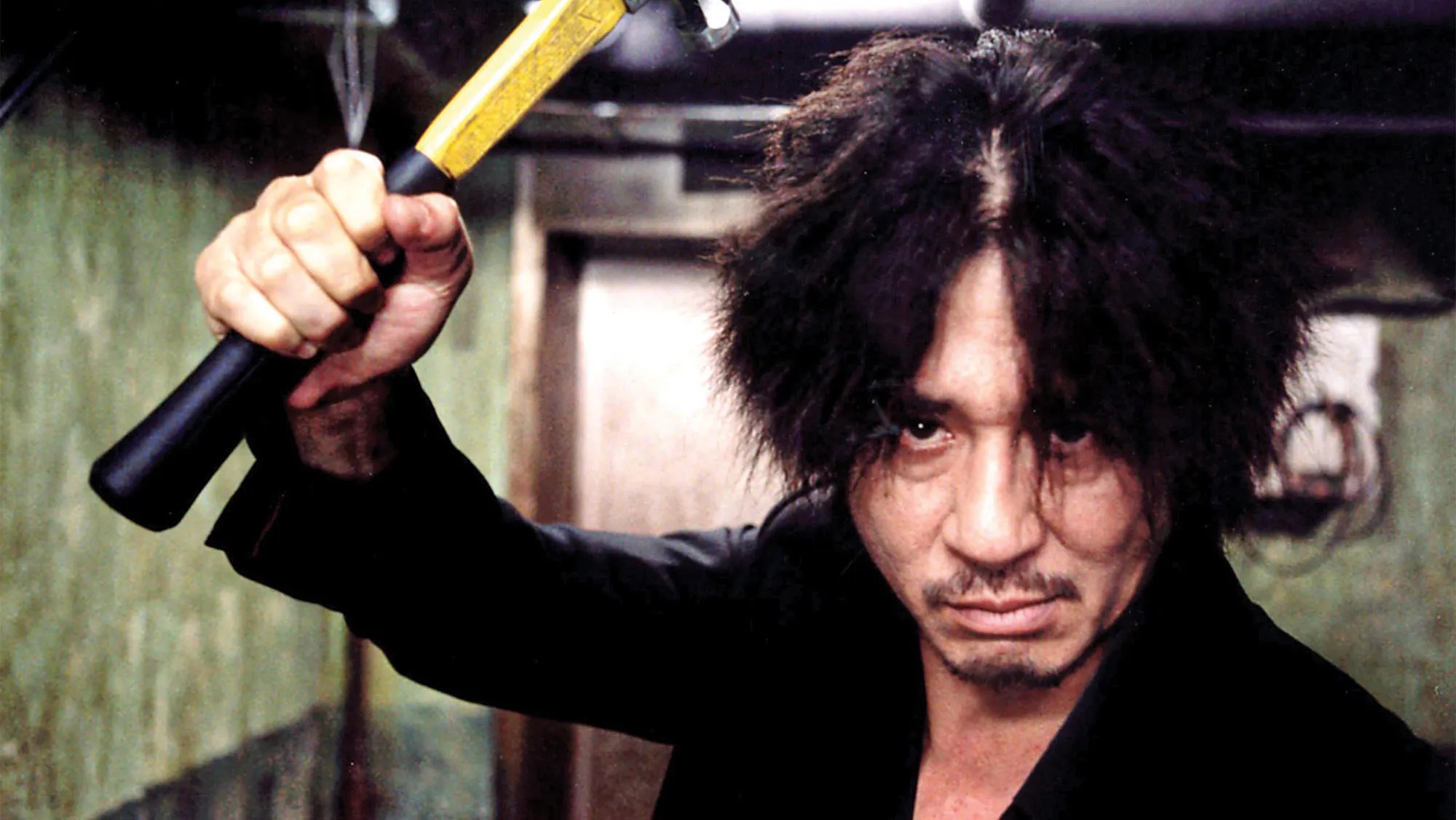 Oh Dae-su (Choi Min-sik), a wild-haired man holding a hammer menacingly over his head, glares into the camera in Oldboy