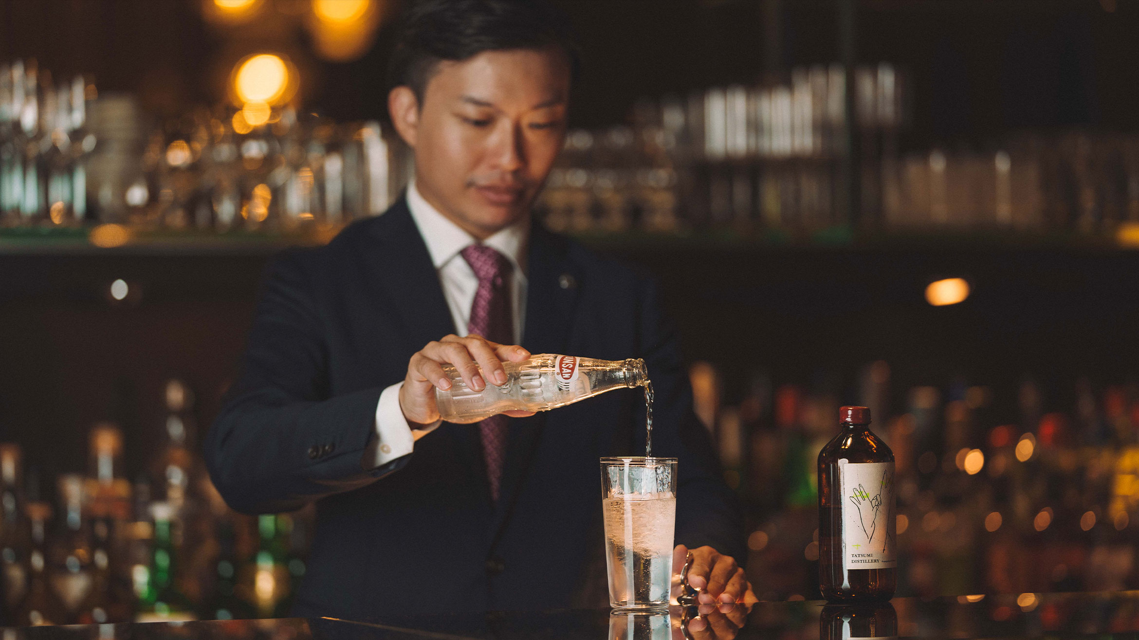 A bartender pours a bottle of tonic into a glass. 