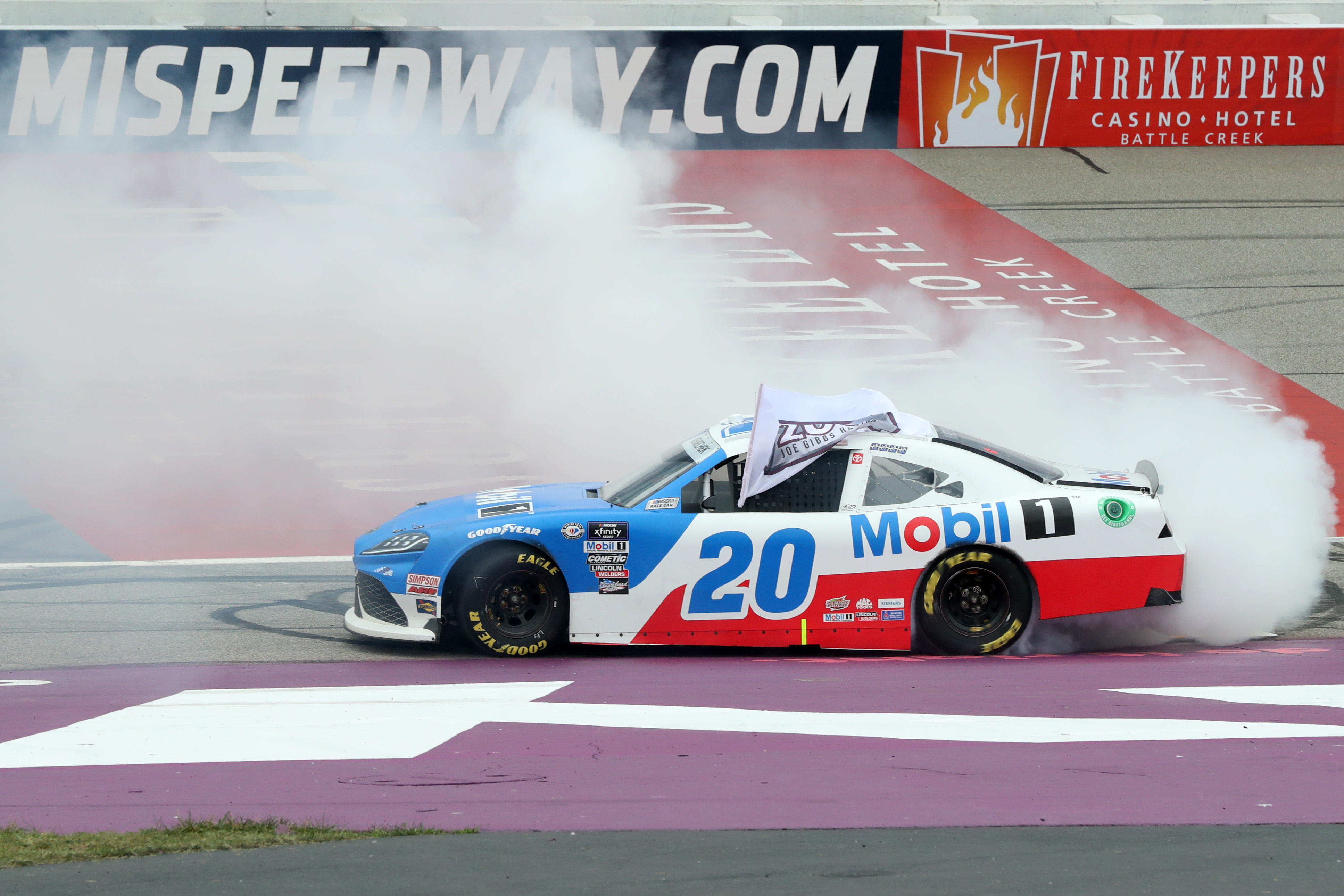 John Hunter Nemechek, driver of the #20 Mobil 1 Toyota, drives with a flag celebrating Joe Gibbs Racing’s 200th NASCAR Xfinity Series win during a burnout after winning the NASCAR Xfinity Series Cabo Wabo 250 at Michigan International Speedway on August 05, 2023 in Brooklyn, Michigan.