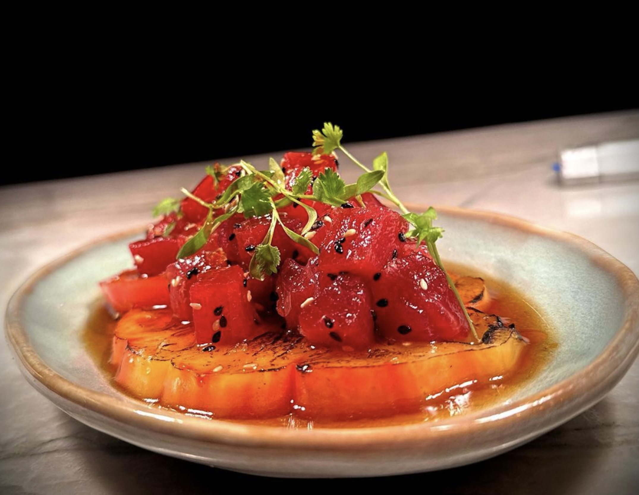 A dish featuring ahi tuna, soy roasted heirloom tomatoes, ponzu, and topped with sesame.