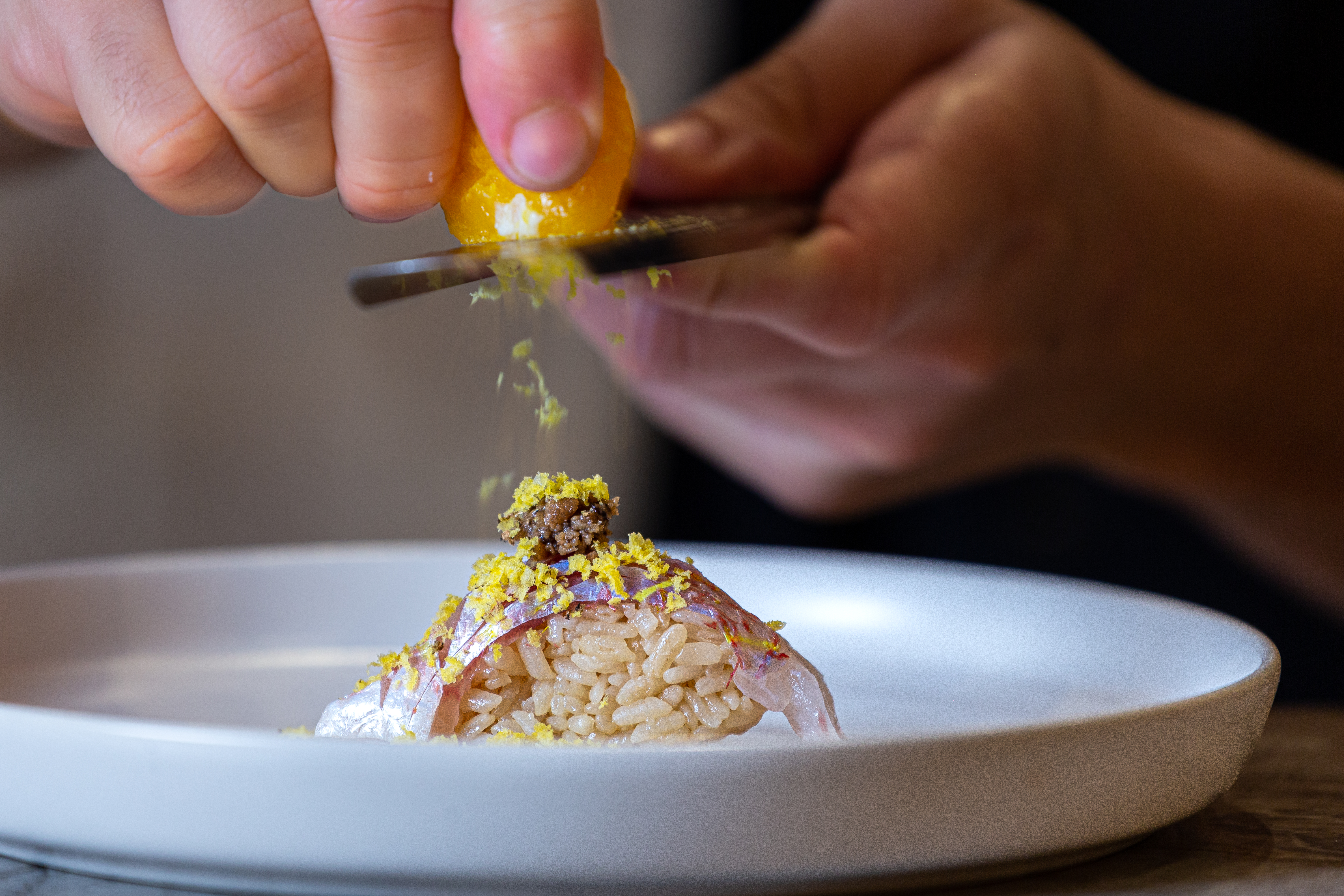 A chef shaves cured egg yolk onto a piece of nigiri at Sushi by Hidden.
