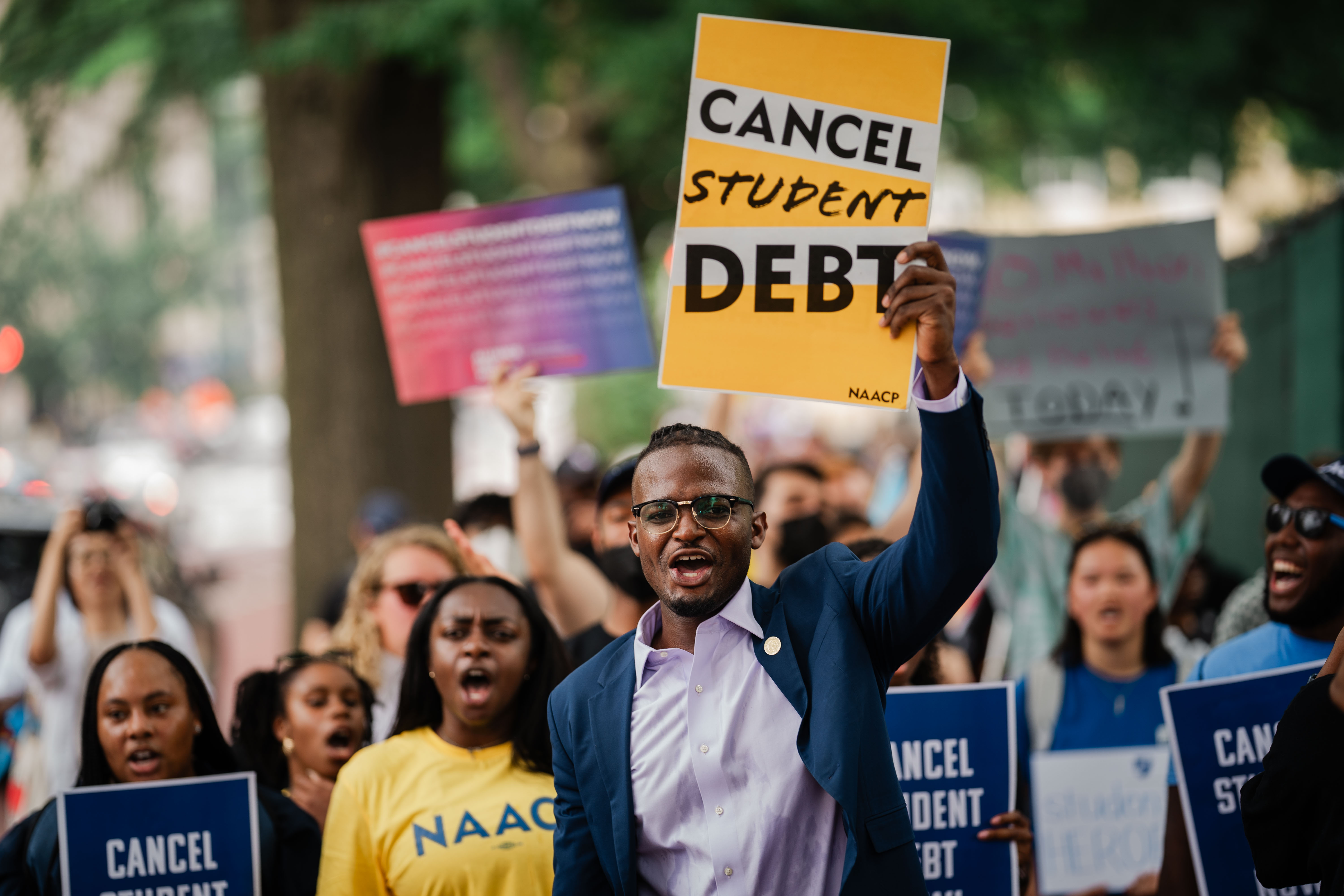 Cole holds a sign that says “Cancel Student Debt” while others march behind him. 
