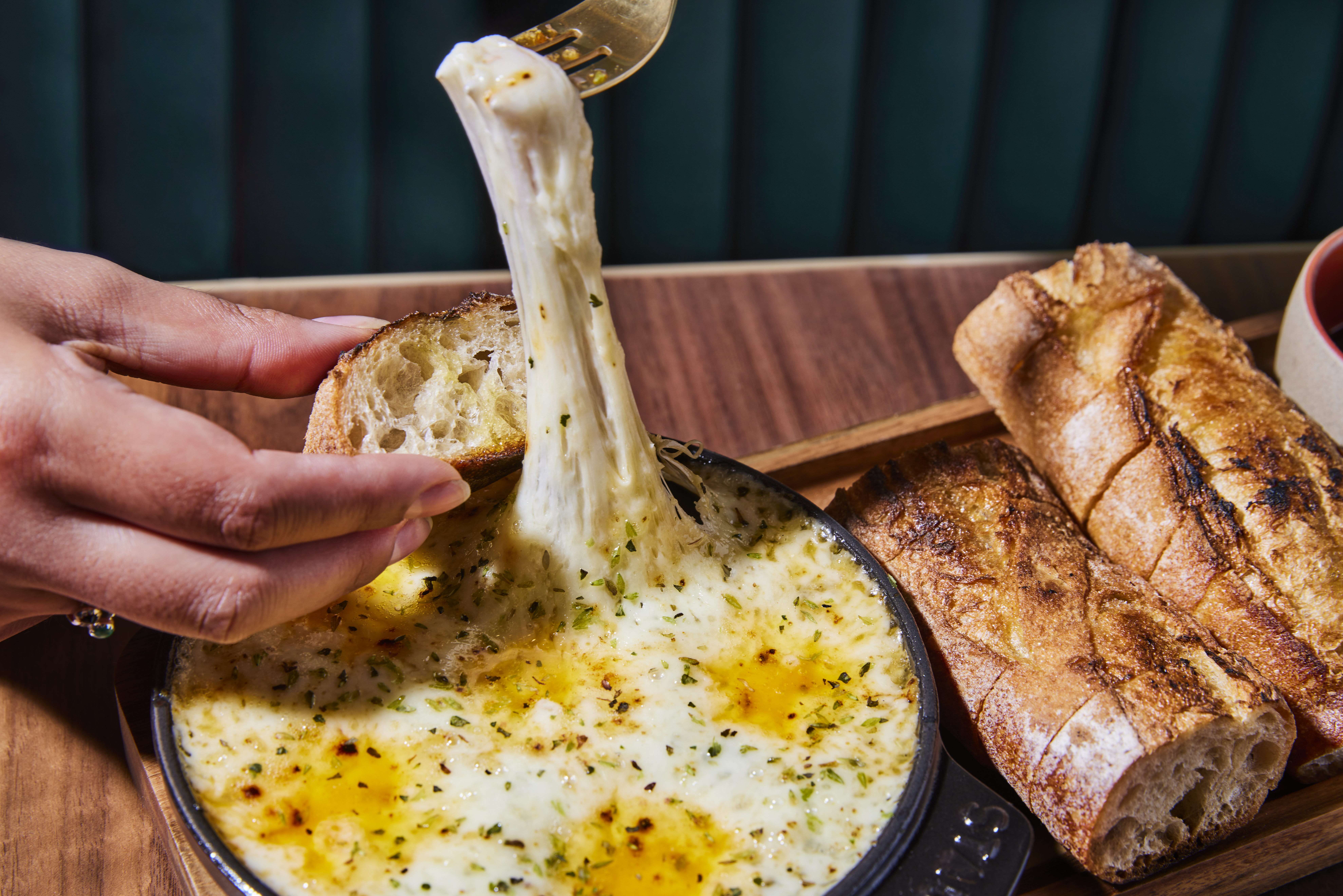 A hand holds bread over a long pull of griddled cheese in a pan at new Que Barbaro in Los Angeles.
