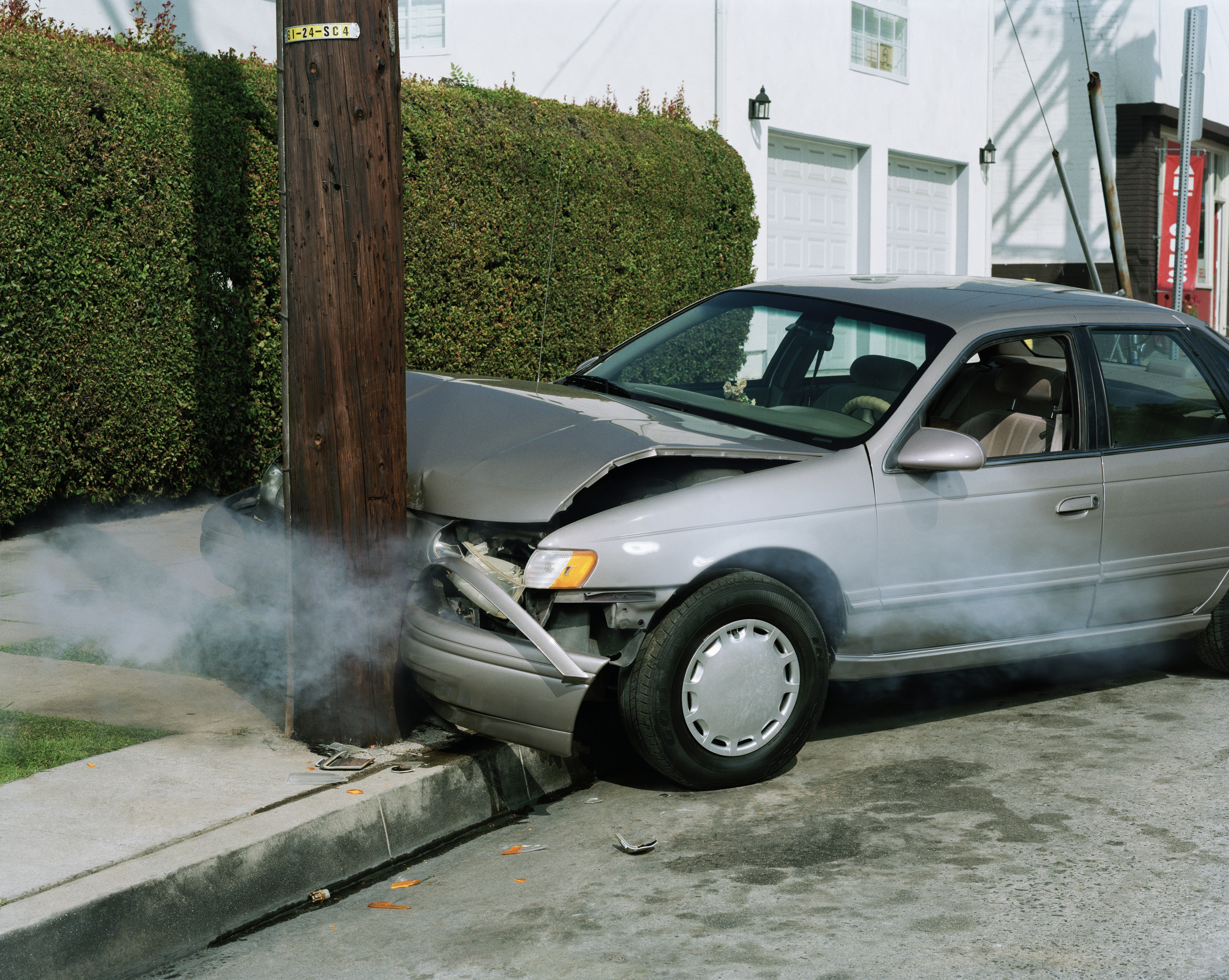 A silver car crashed into a wooden utility pole on the side of a residential street, its hood bent in and steam rolling from its engine.