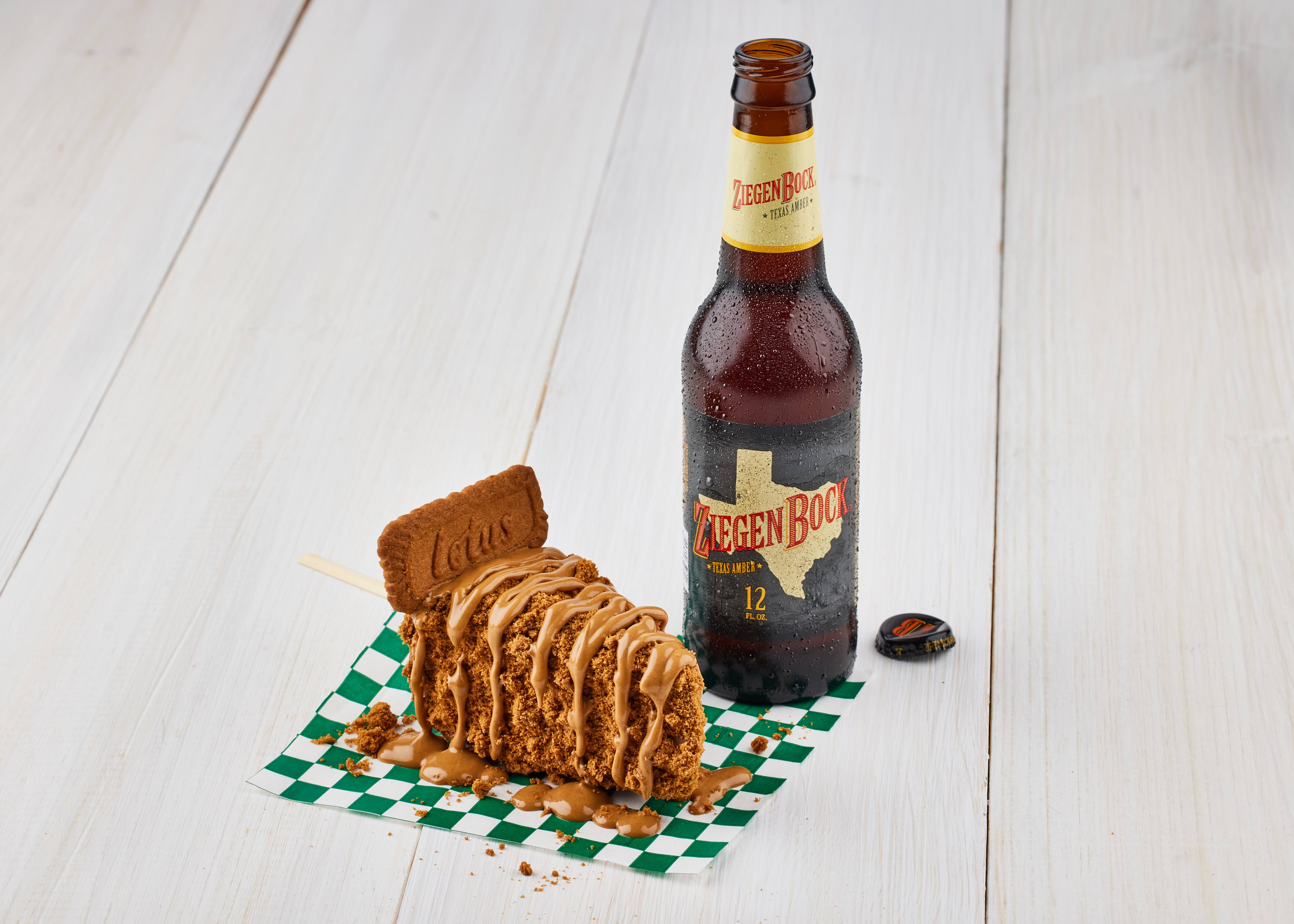 A slice of cheesecake is covered in brown sauce and cookie crumbles. To the right is a bottle of beer.