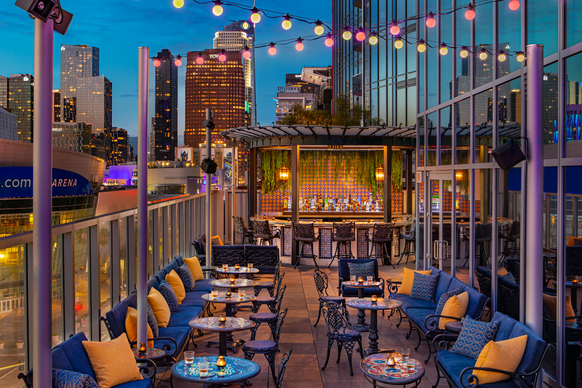 Colorful dusk-lit rooftop patio of Mother of Pearl with wrought iron seating and blue banquettes.