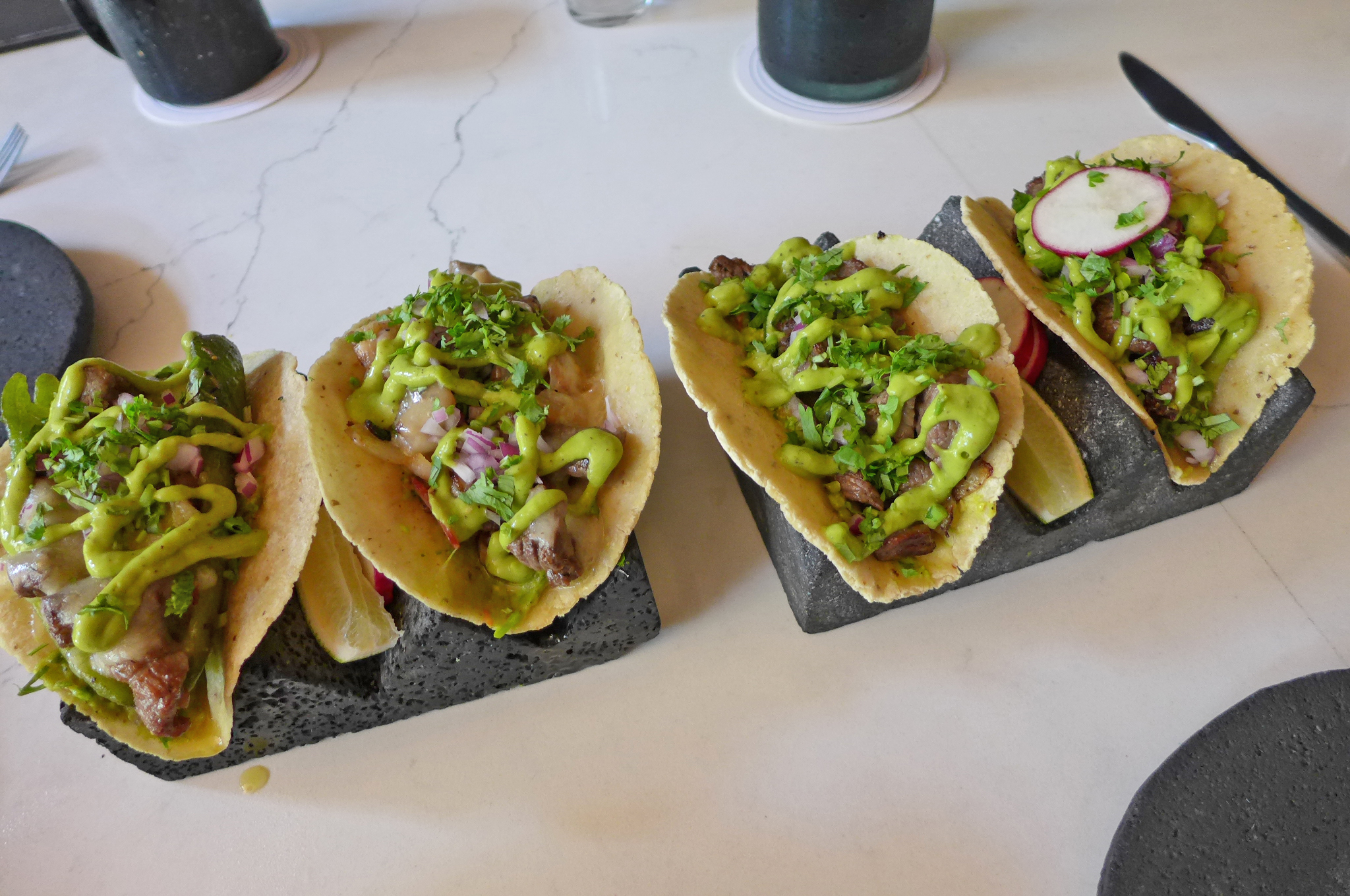 Four tacos squiggled with guacamole on a taco rack.