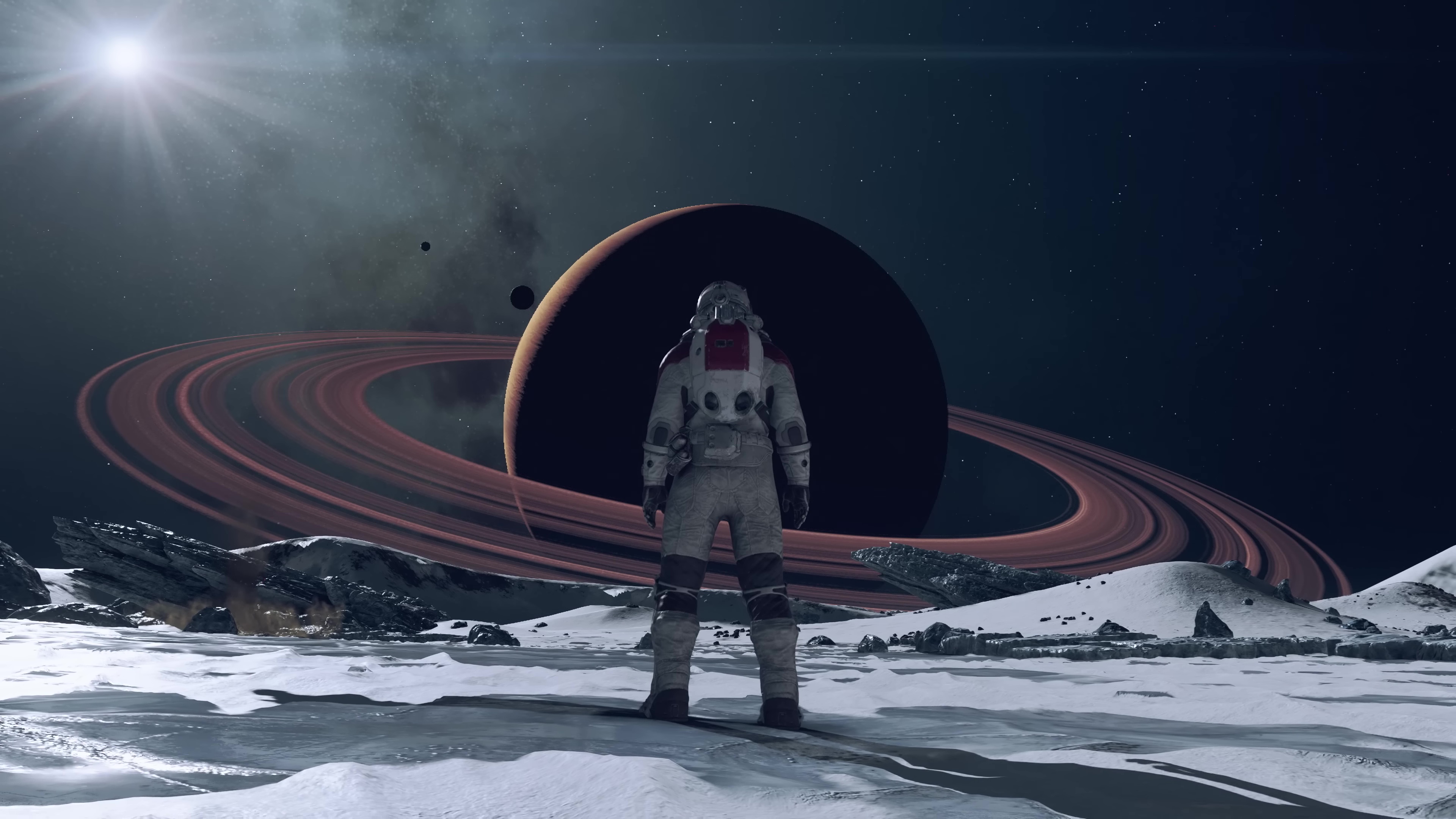 in a screenshot from Starfield, an astronaut, seen from behind, stands on an icy planet and looks toward a Saturn-like ringed planet in the distance, with a sunlike star shining in the upper left corner