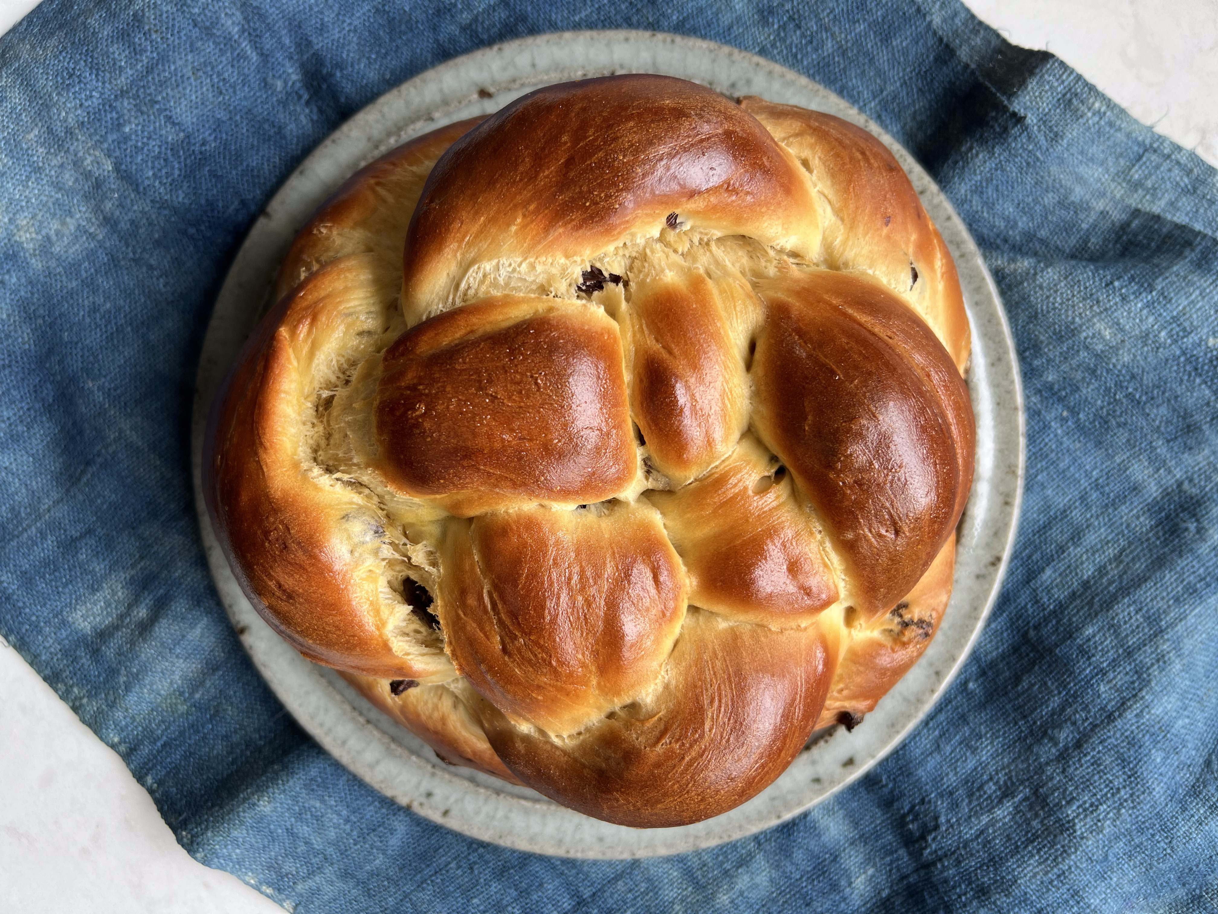 A round loaf of braided challah sitting on top of a plate and a blue napkin.