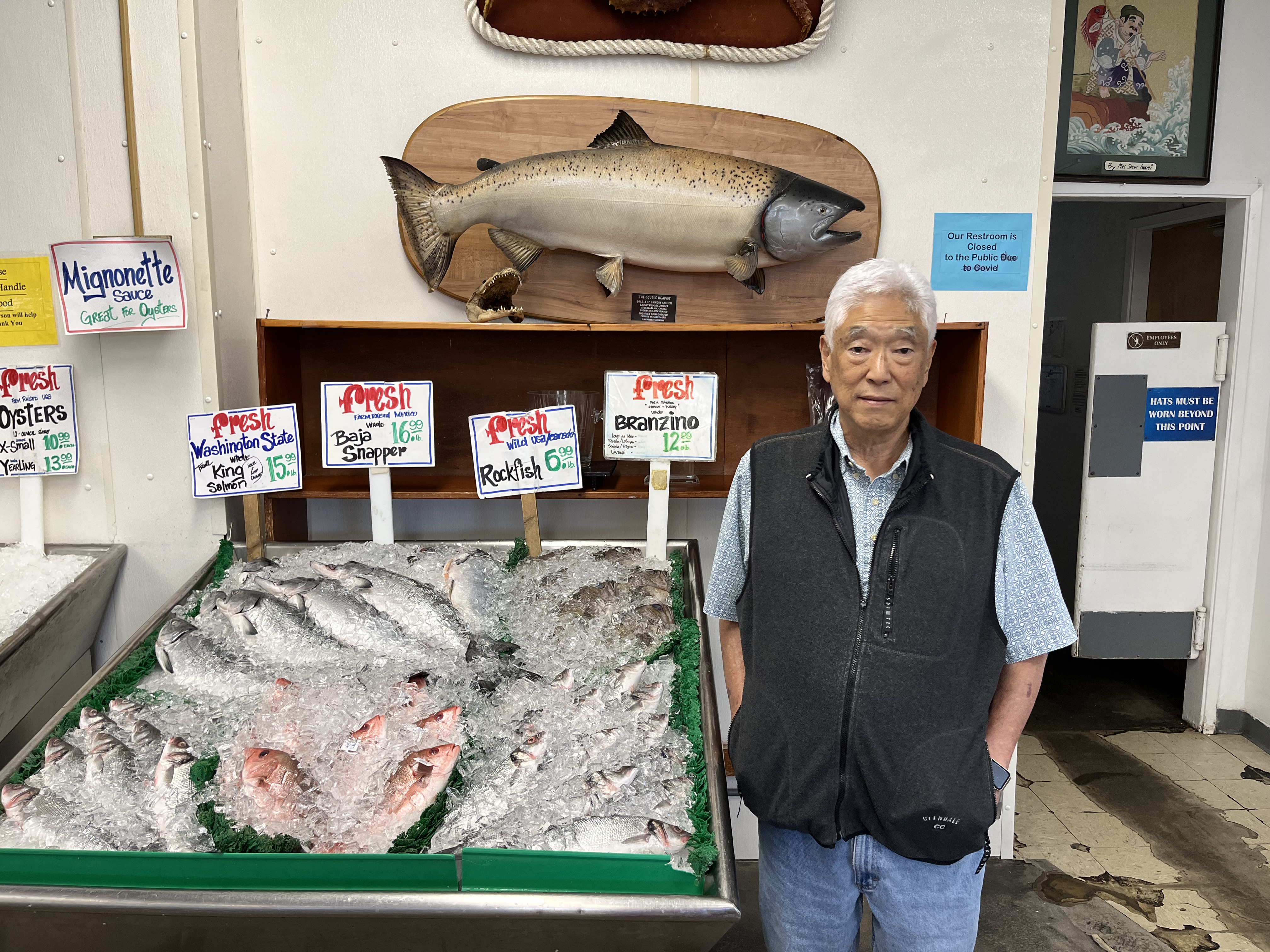 An Asian man standing in front of a display of fish on ice.