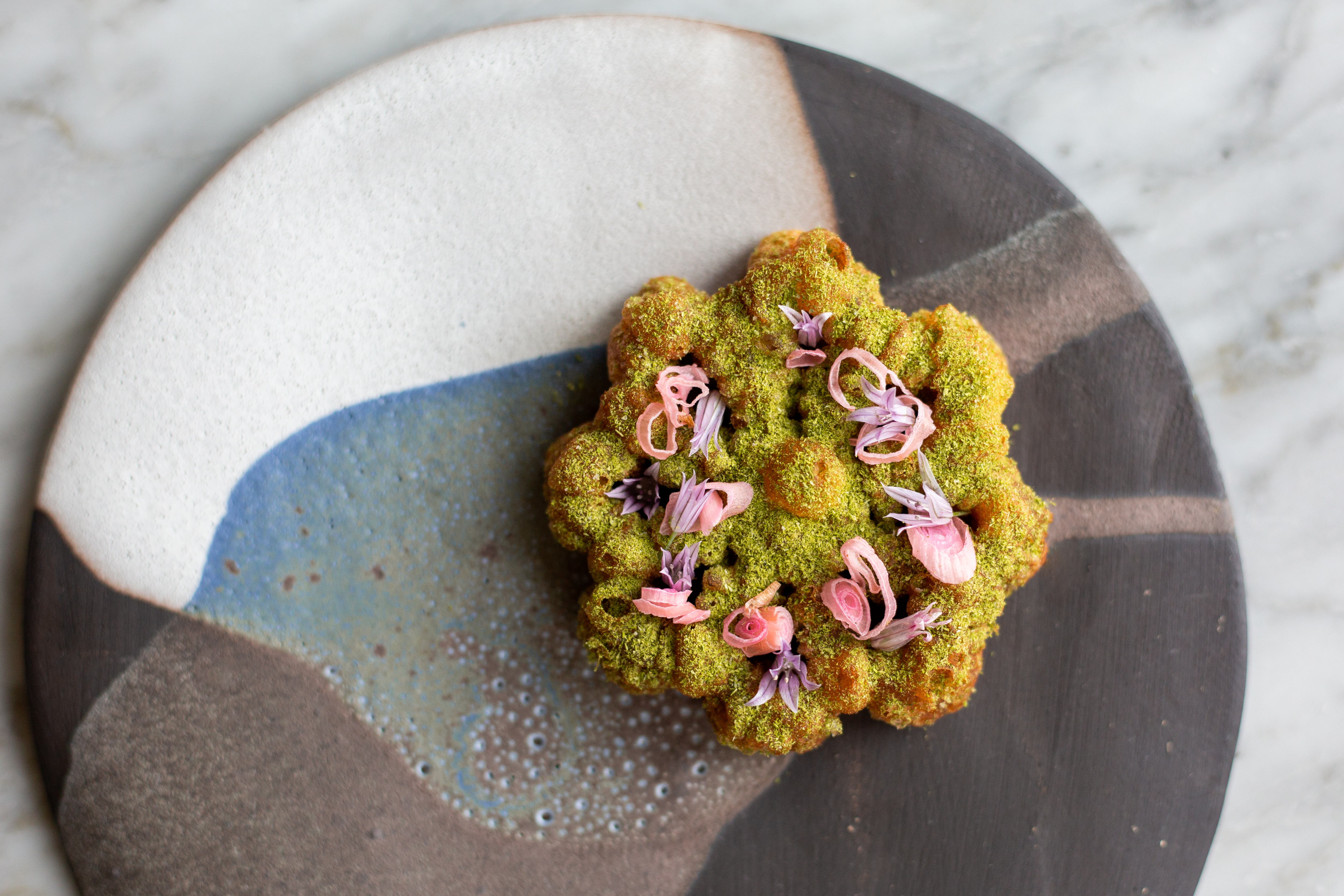 A cookie dusted with green dust and flower petals artfully plated.