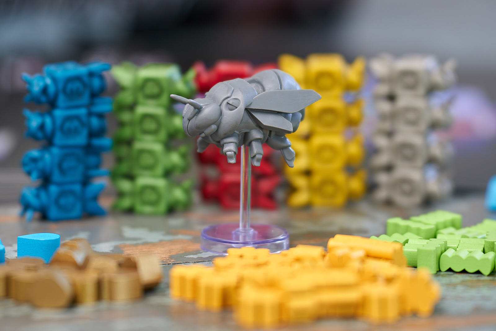 A queen bee pawn, in gray plastic, backed by dozens of colony ships and worker bee tokens. They are all miniatures from Apiary, a new game from Stonemaier Games.