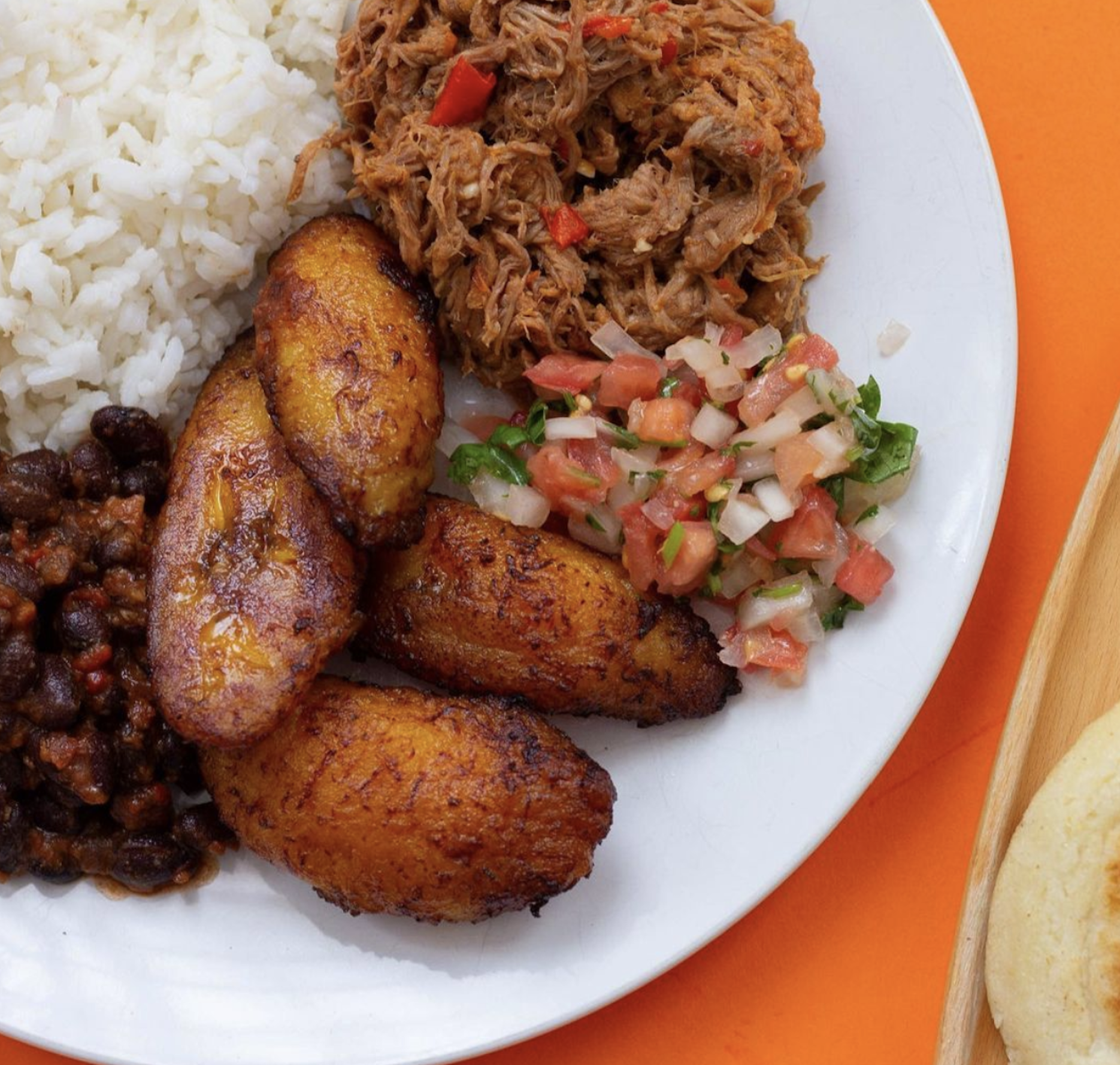 A platter that includes plantains, shredded beef, with fresh pico de gallo on top alongside white rice. 