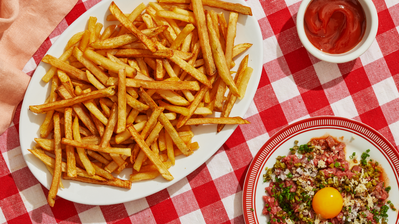 An overhead view of a plate of French fries and another plate of beef tartare.
