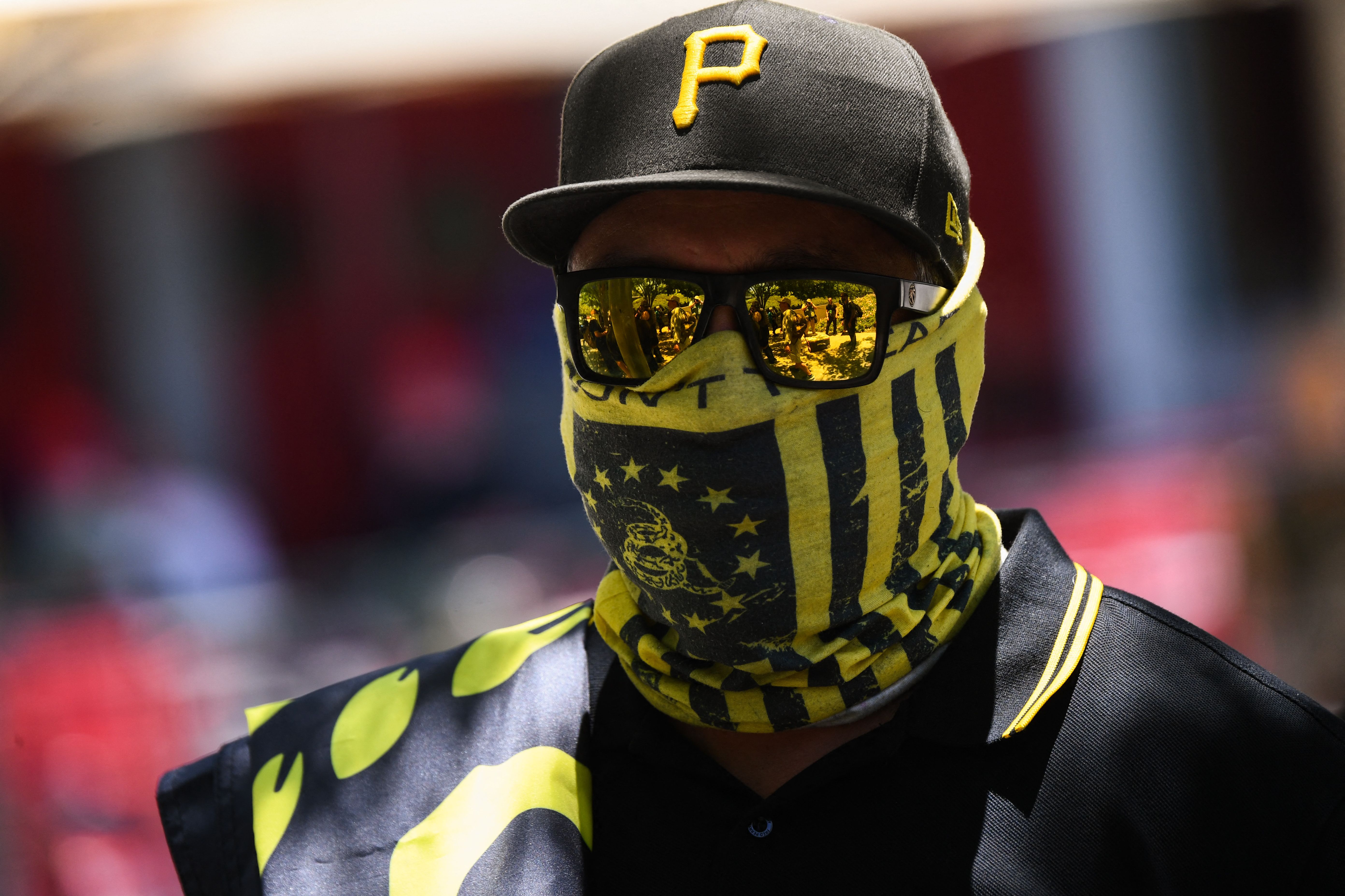 A man in a black baseball cap with a yellow “P,” a black and yellow face covering, and black and yellow reflective sunglasses.