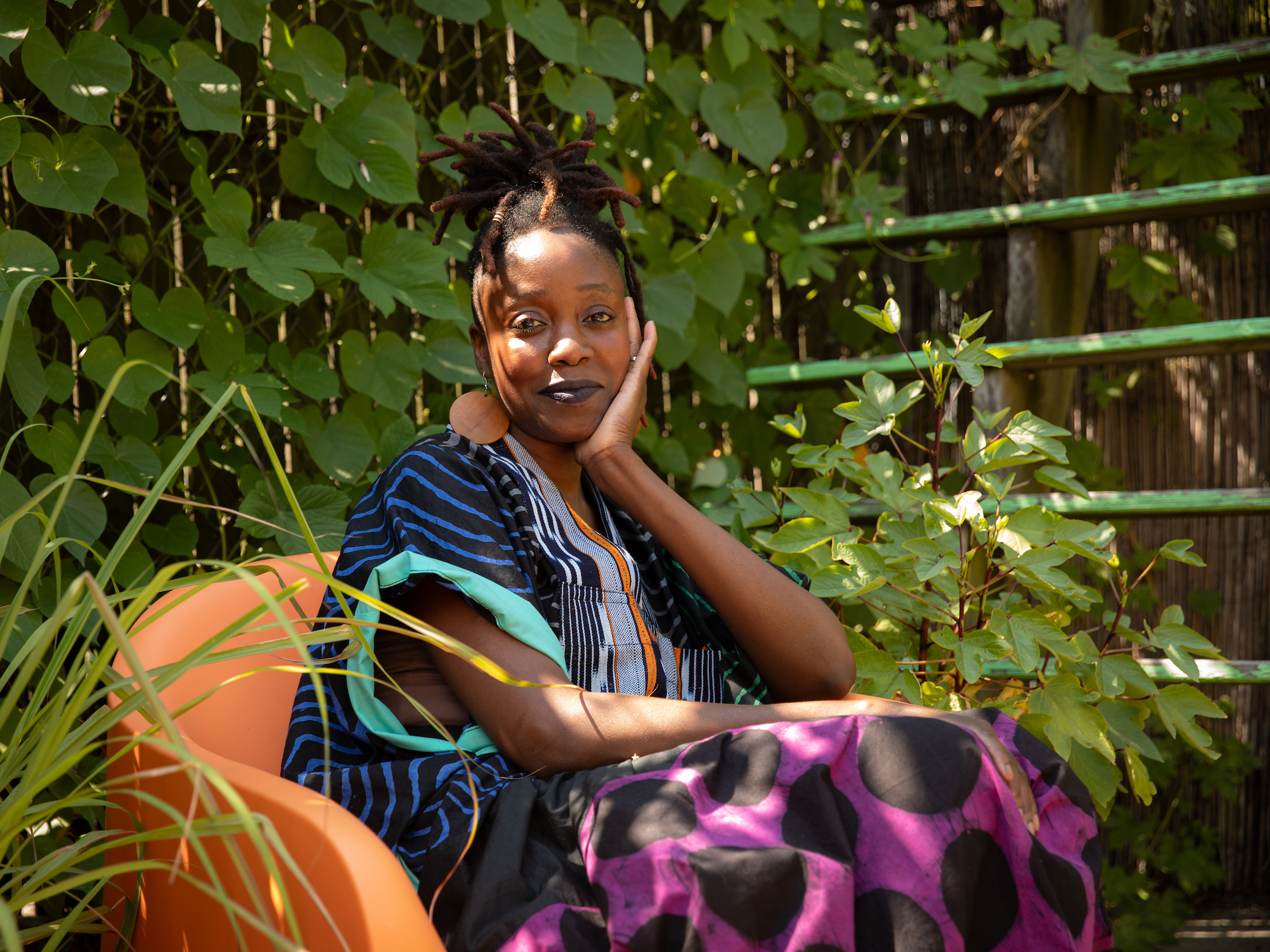 Yewande Komolafe sits in an orange chair, surrounded by plants.