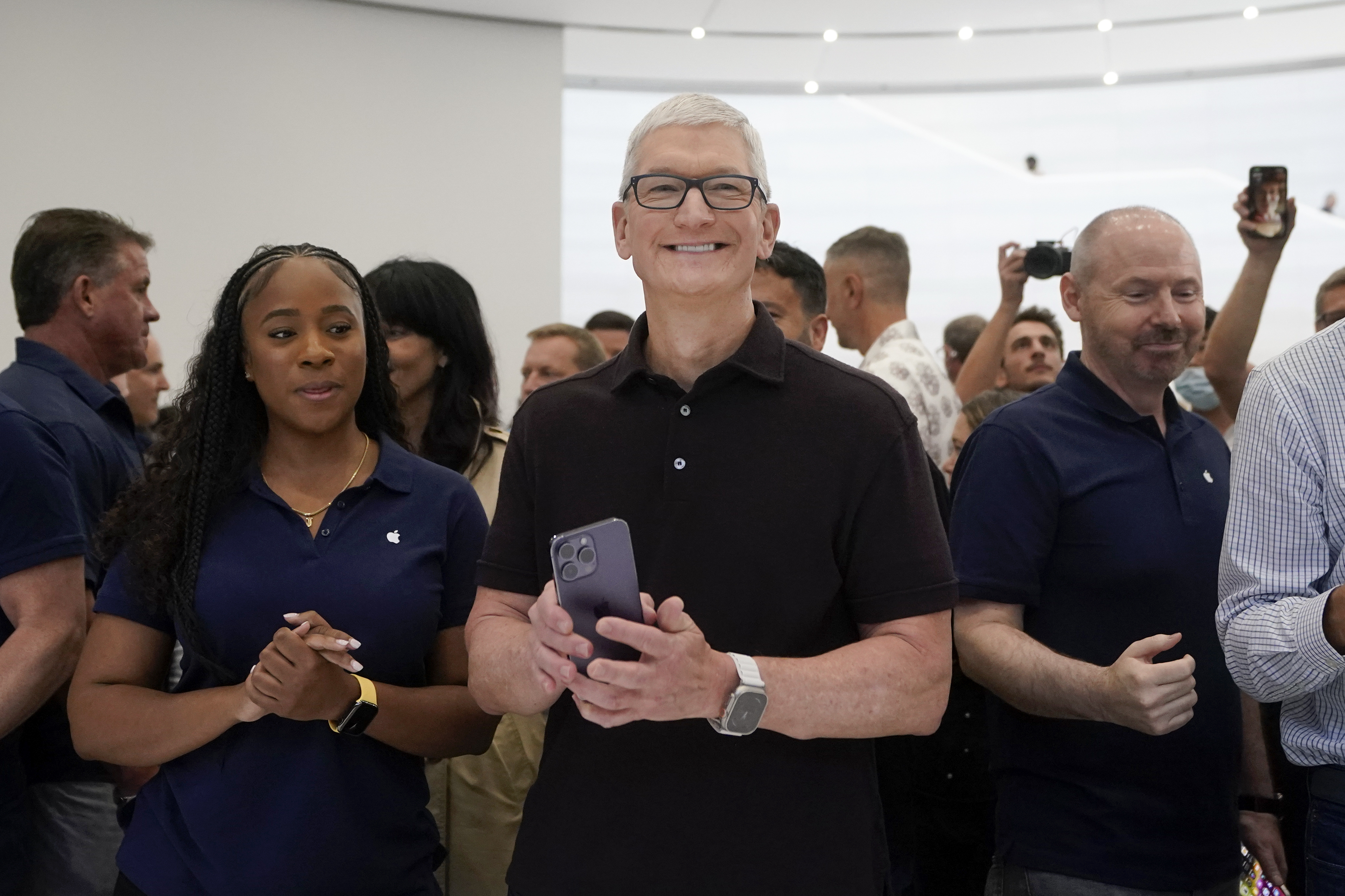Apple CEO Tim Cook smiling and holding an iPhone.