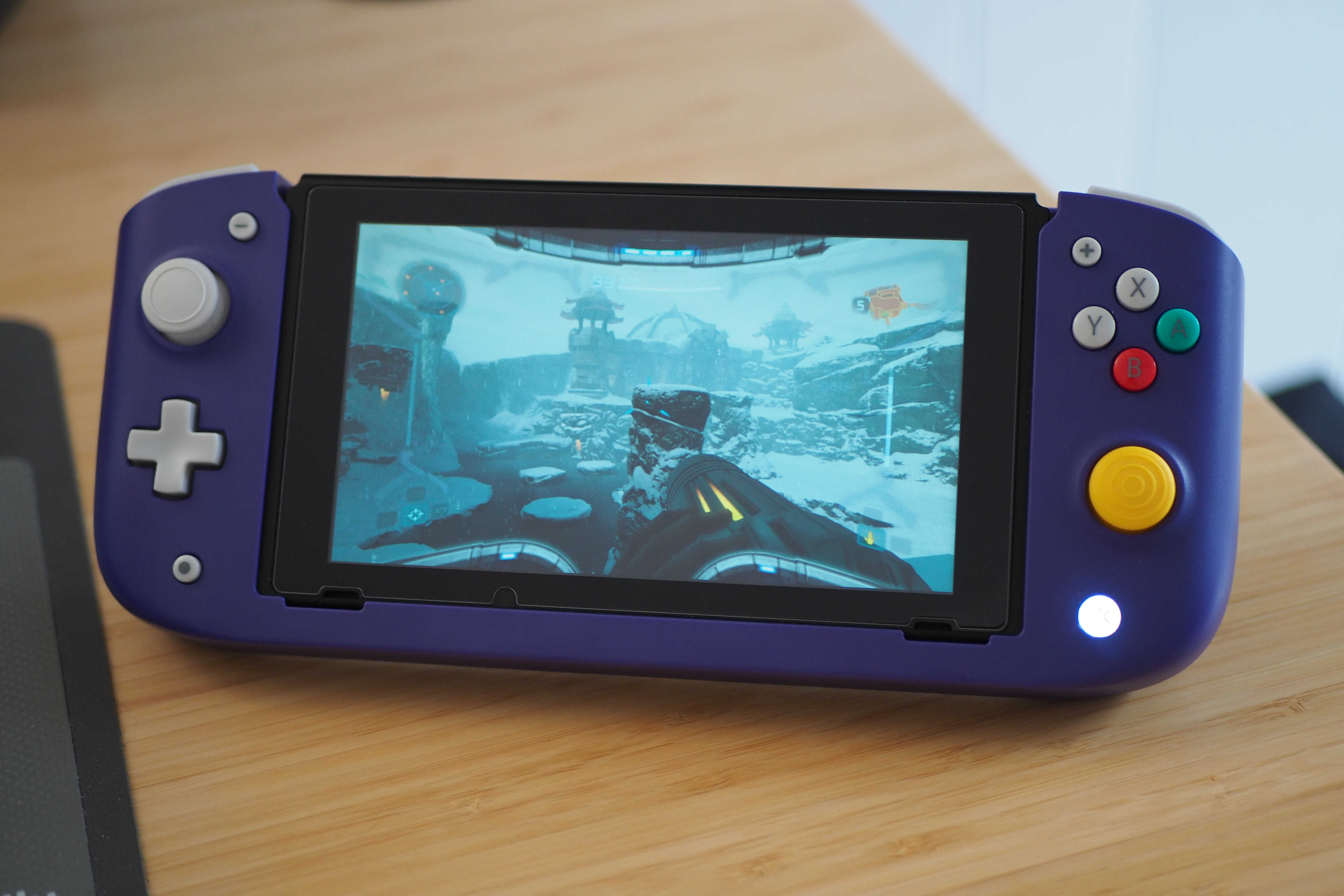 An image of the CRKD Nitro Deck in the GameCube color scheme. The Nintendo Switch accessory is holding a Switch, which is displaying Metroid Prime: Remastered on its screen.