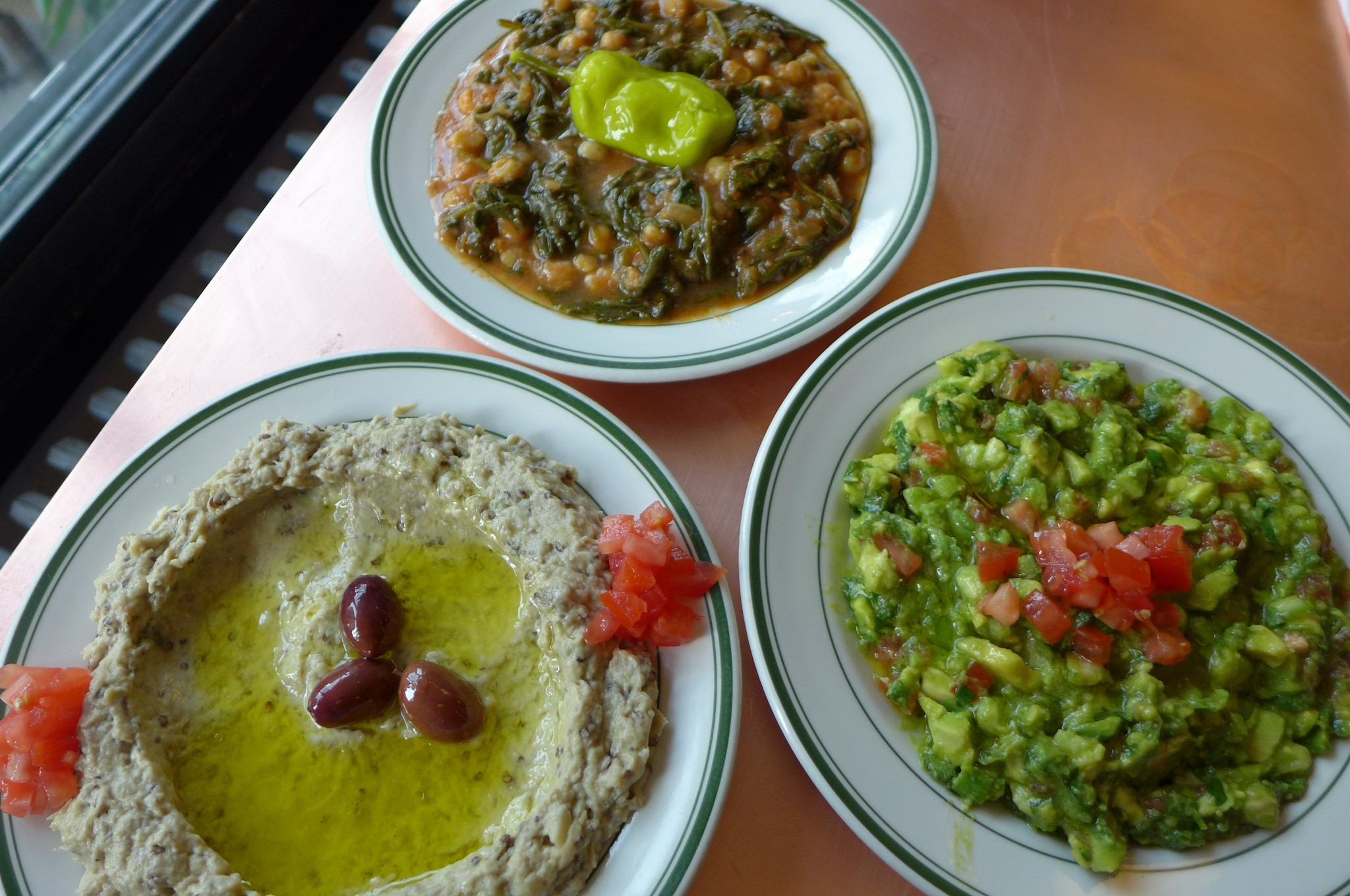 Three plates of babaghanoush, beans and spinach, and minced avocado.