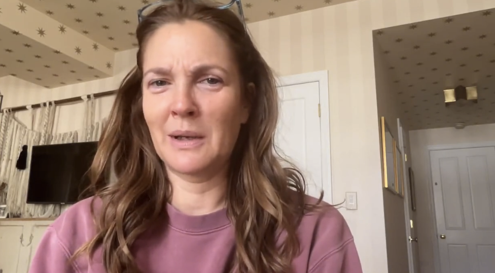 Drew Barrymore without makeup, in a casual sweatshirt, filming her apology video from home. 