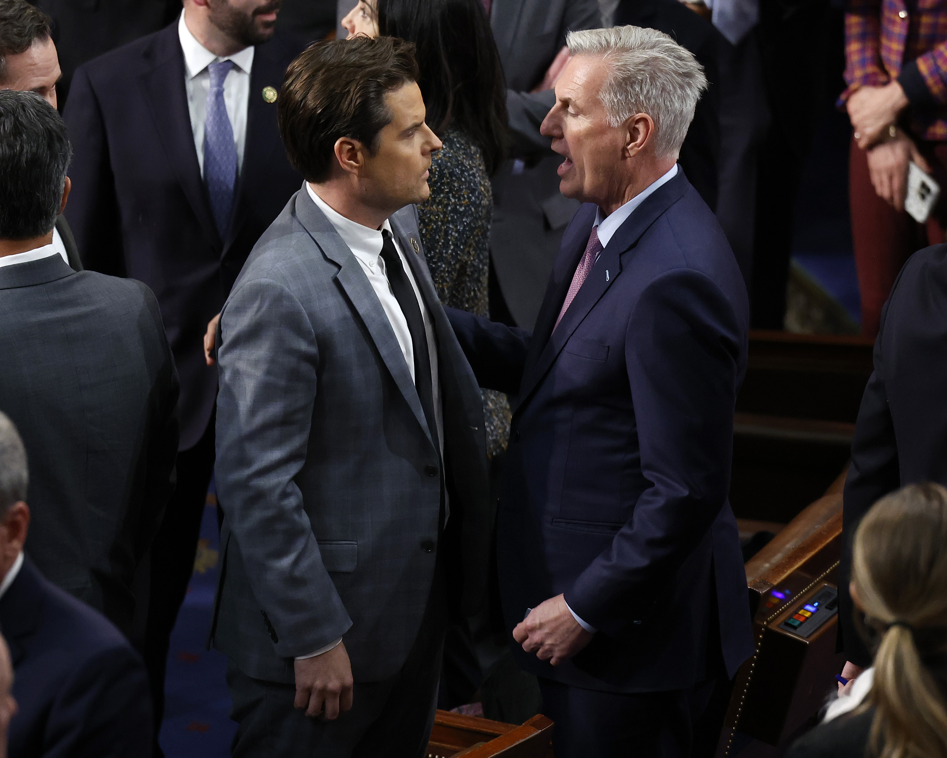 Kevin McCarthy, right, in a blue suit, speaks with Matt Gaetz, left, in a gray suit, surrounded by others on the House floor.