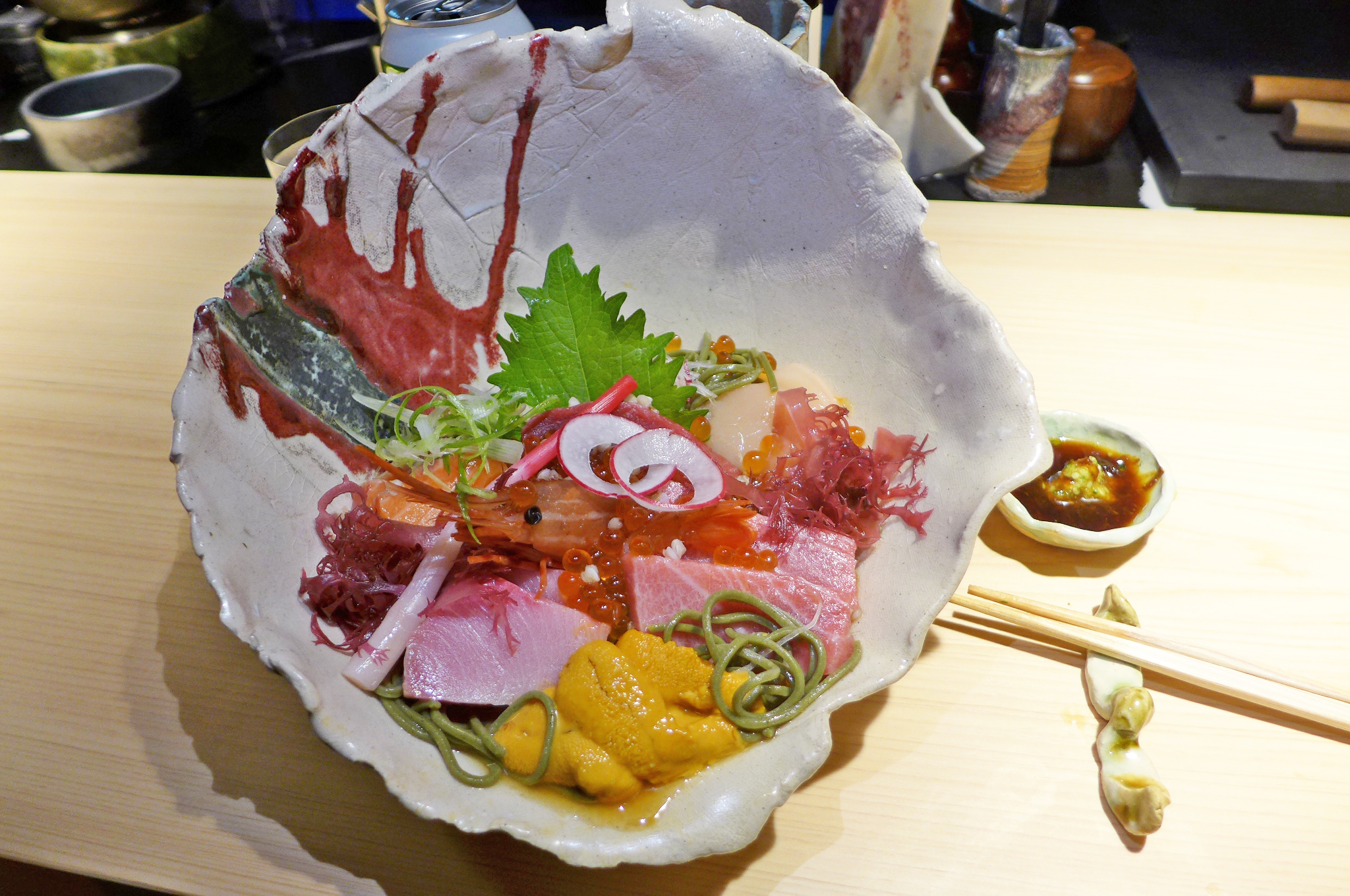 Raw fish in a white conical bowl with green noodle peeping out underneath.