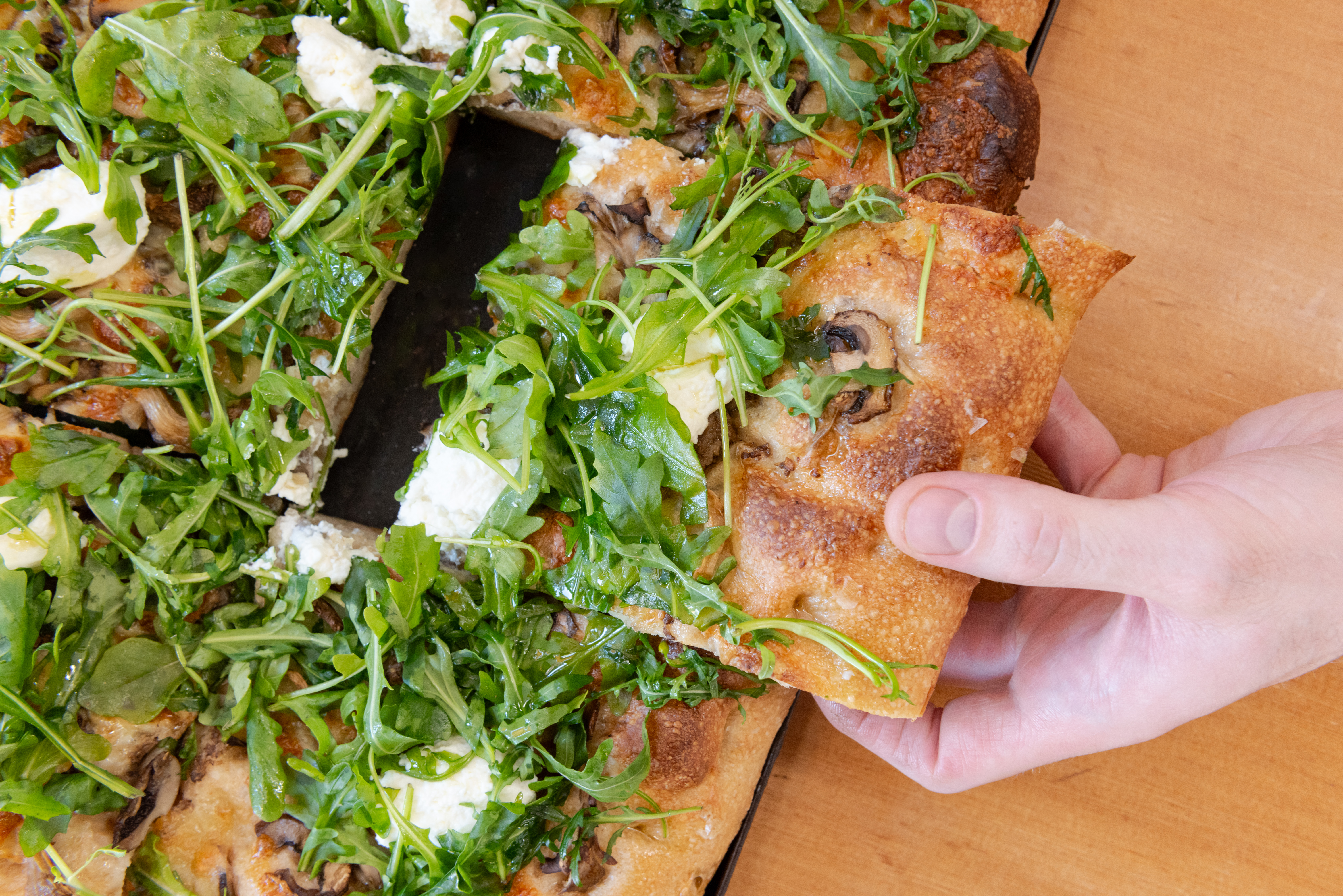 A hand pulls a piece of focaccia from a full slab at Montelupo in Portland, Oregon.