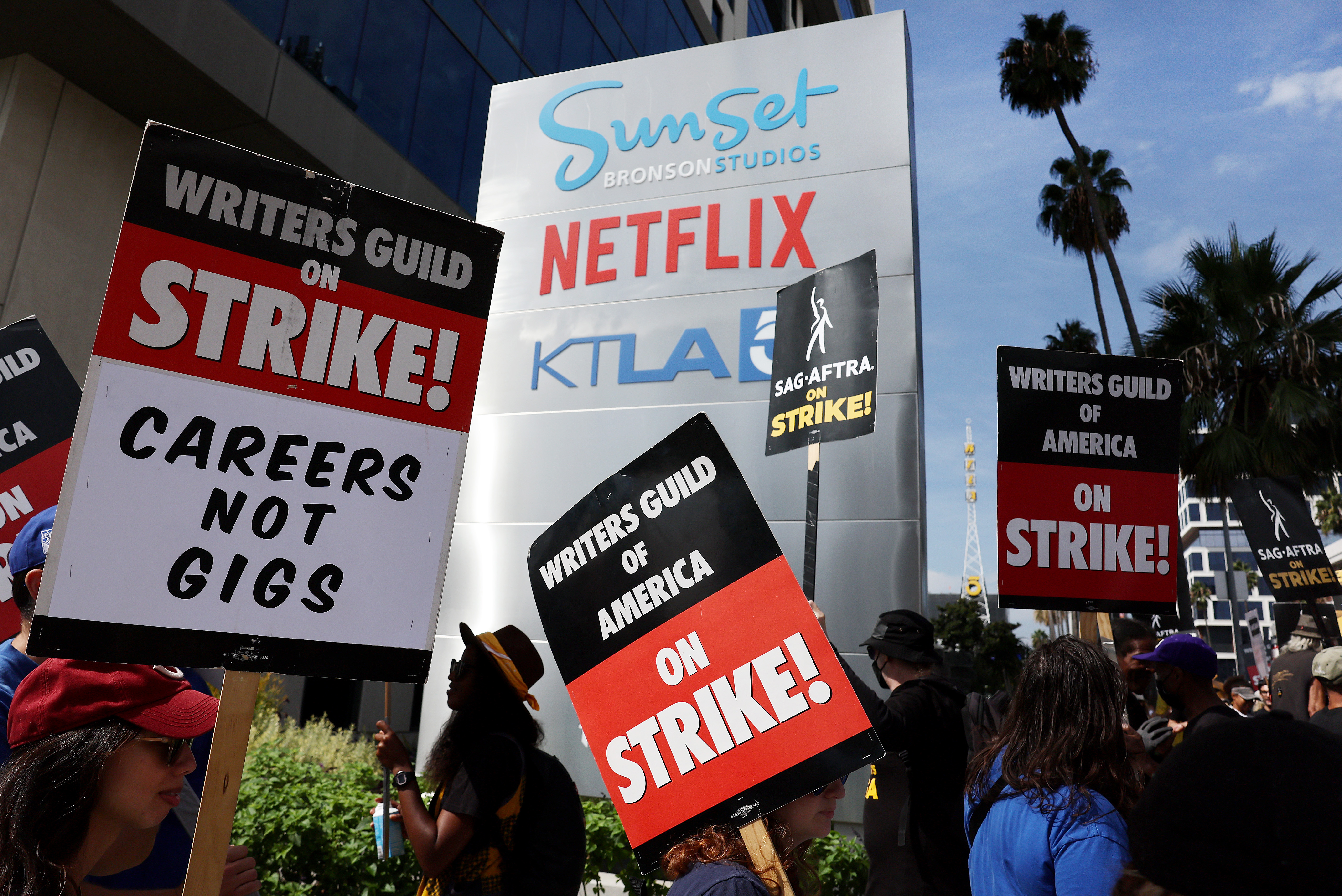 Writers Guild of America members picket near a sign for Netflix and KTLA. Their signs say “Writers Guild on strike!” and “Careers not gigs.”