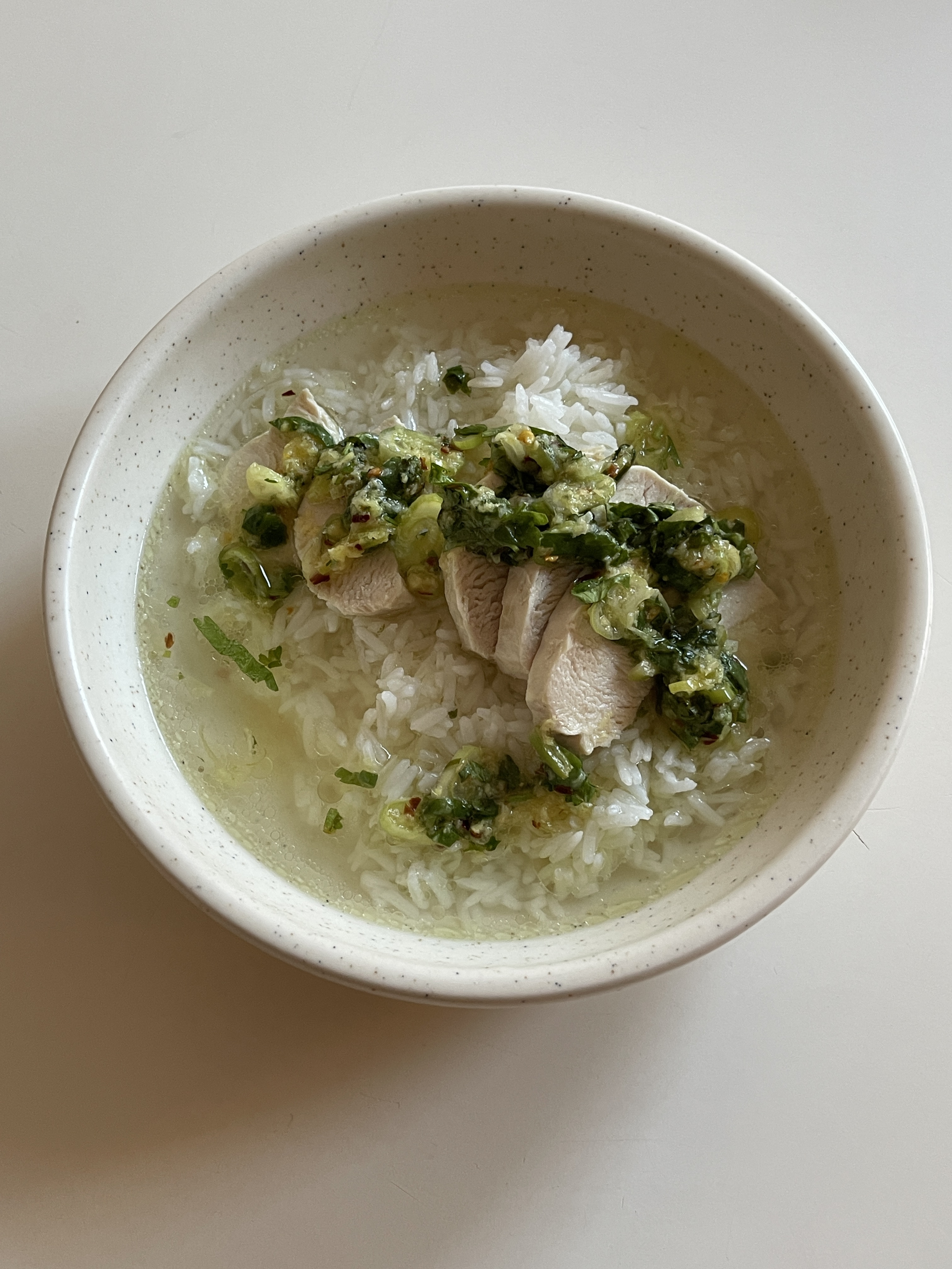 A bowl of poached chicken with brothy rice and cilantro scallion sauce