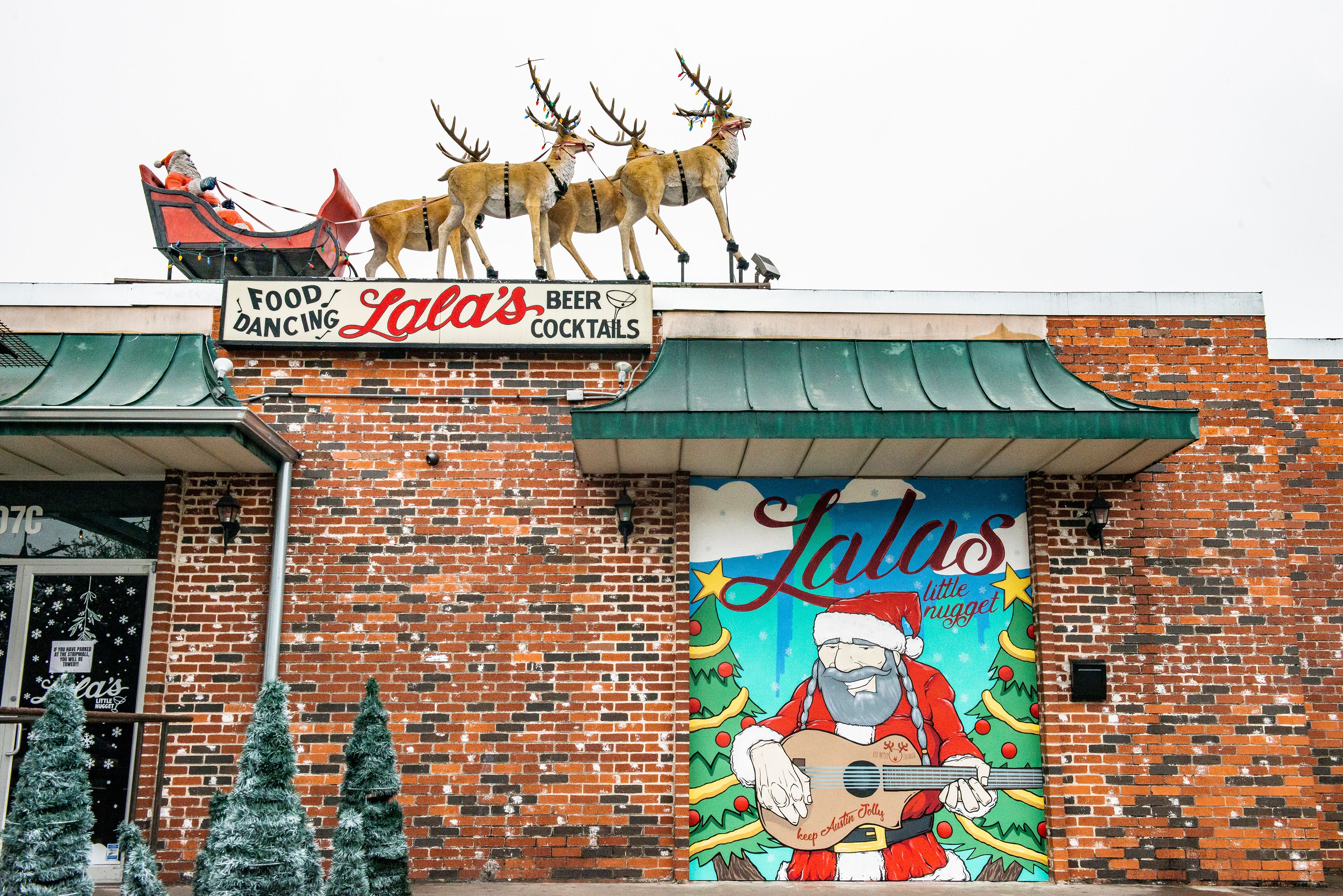 A bar exterior with fake Santa and reindeer in a sleigh above and a mural of Santa playing a guitar.