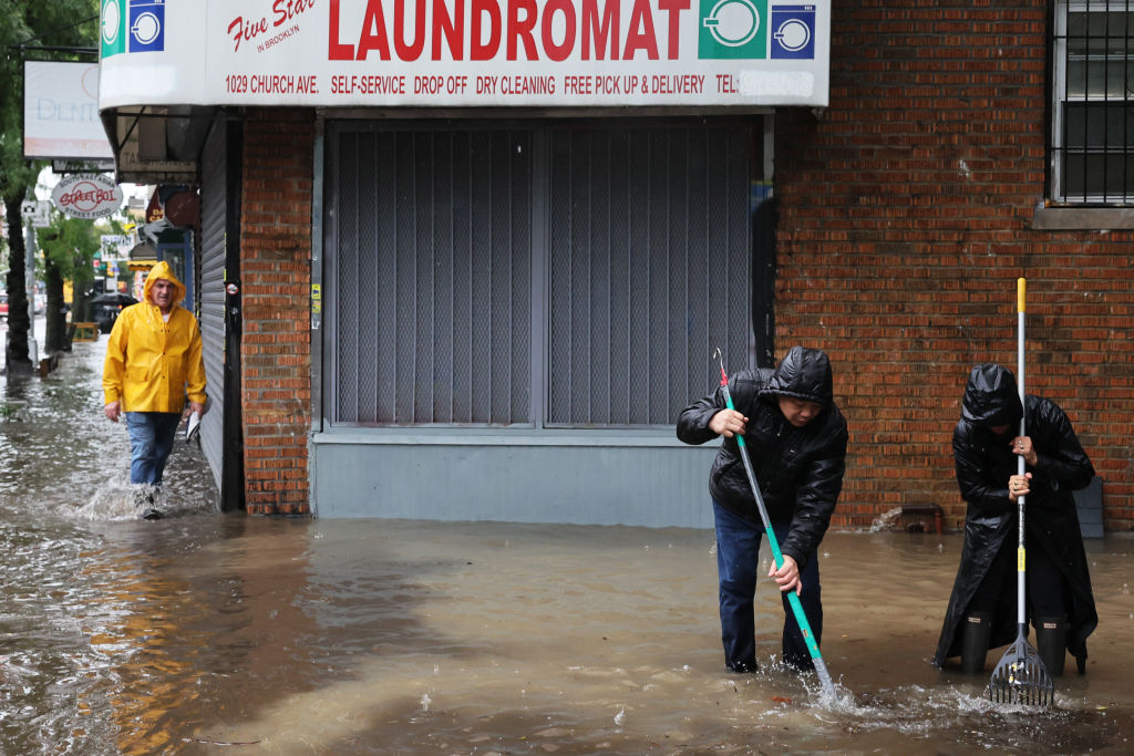 Two men attempt to clear deep flood water from in front of a New York City laundromat