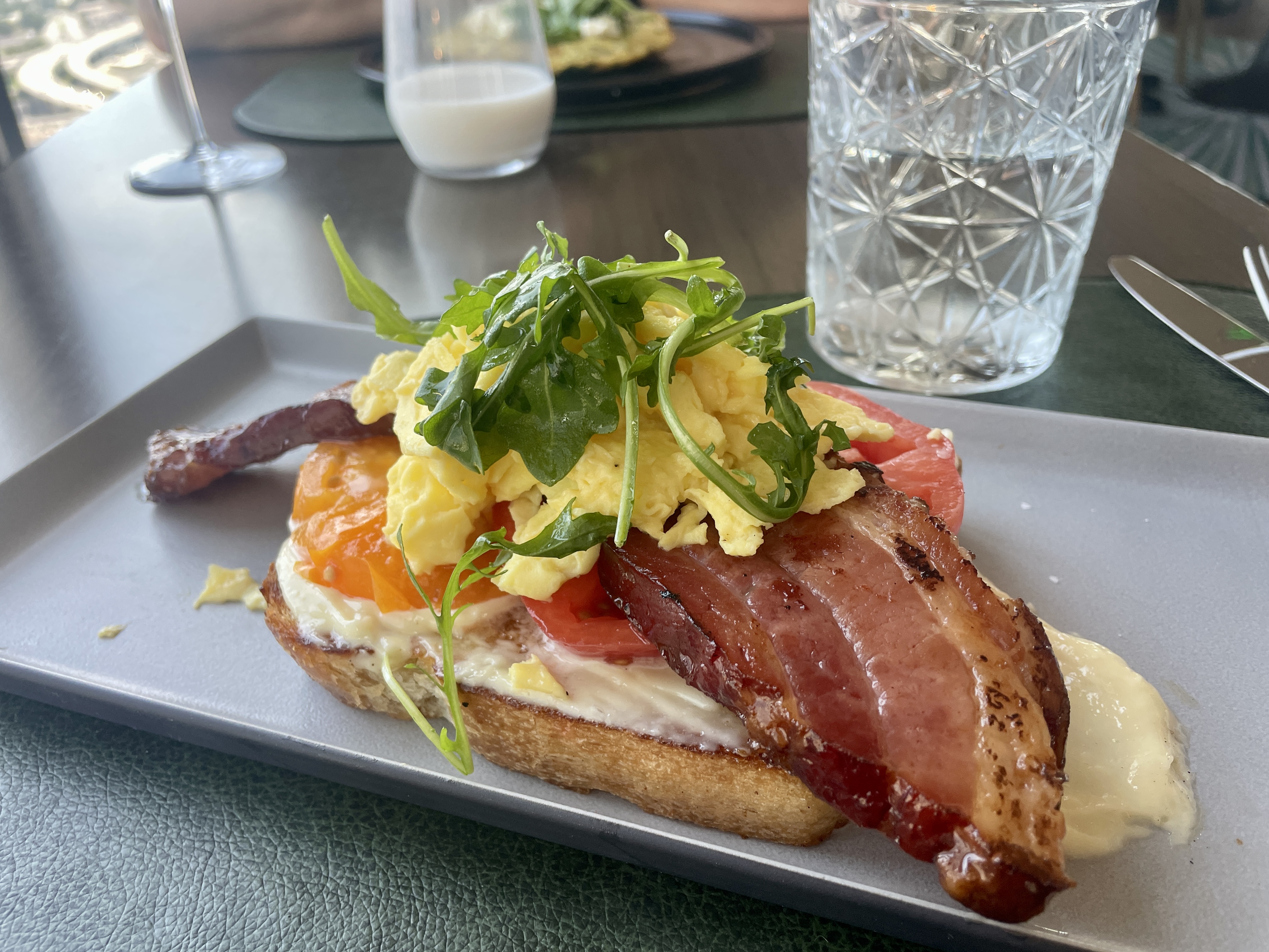 A plate holds a piece of toast with eggs, bacon, tomatoes, and lettuce.