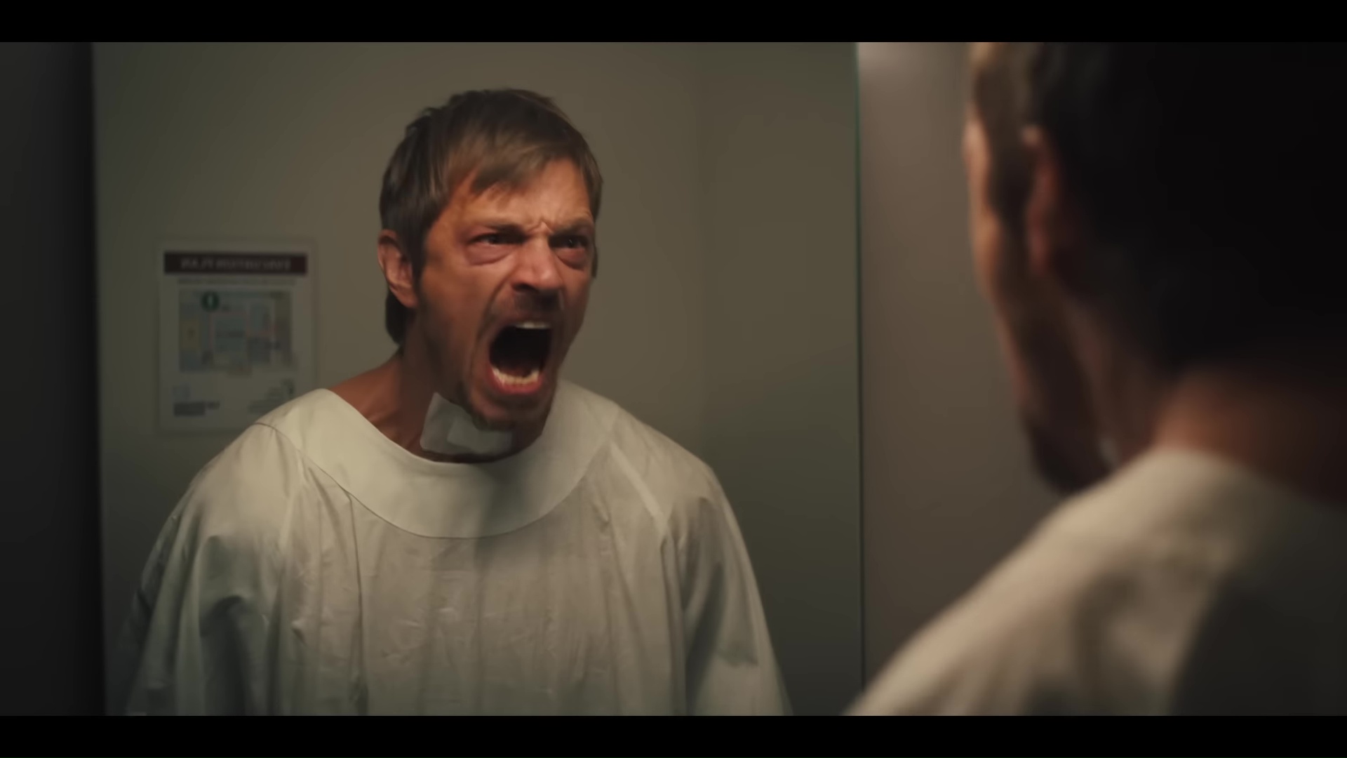 Joel Kinnaman yells into a mirror in a hospital gown with a bandage over his throat in the trailer for Silent Night