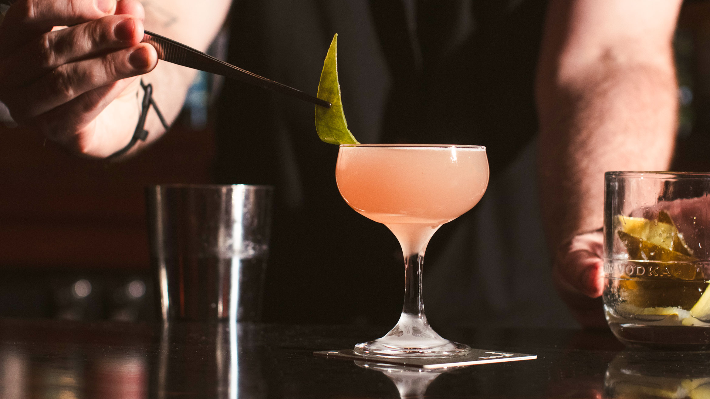 A bartender garnishes a cocktail with leaf