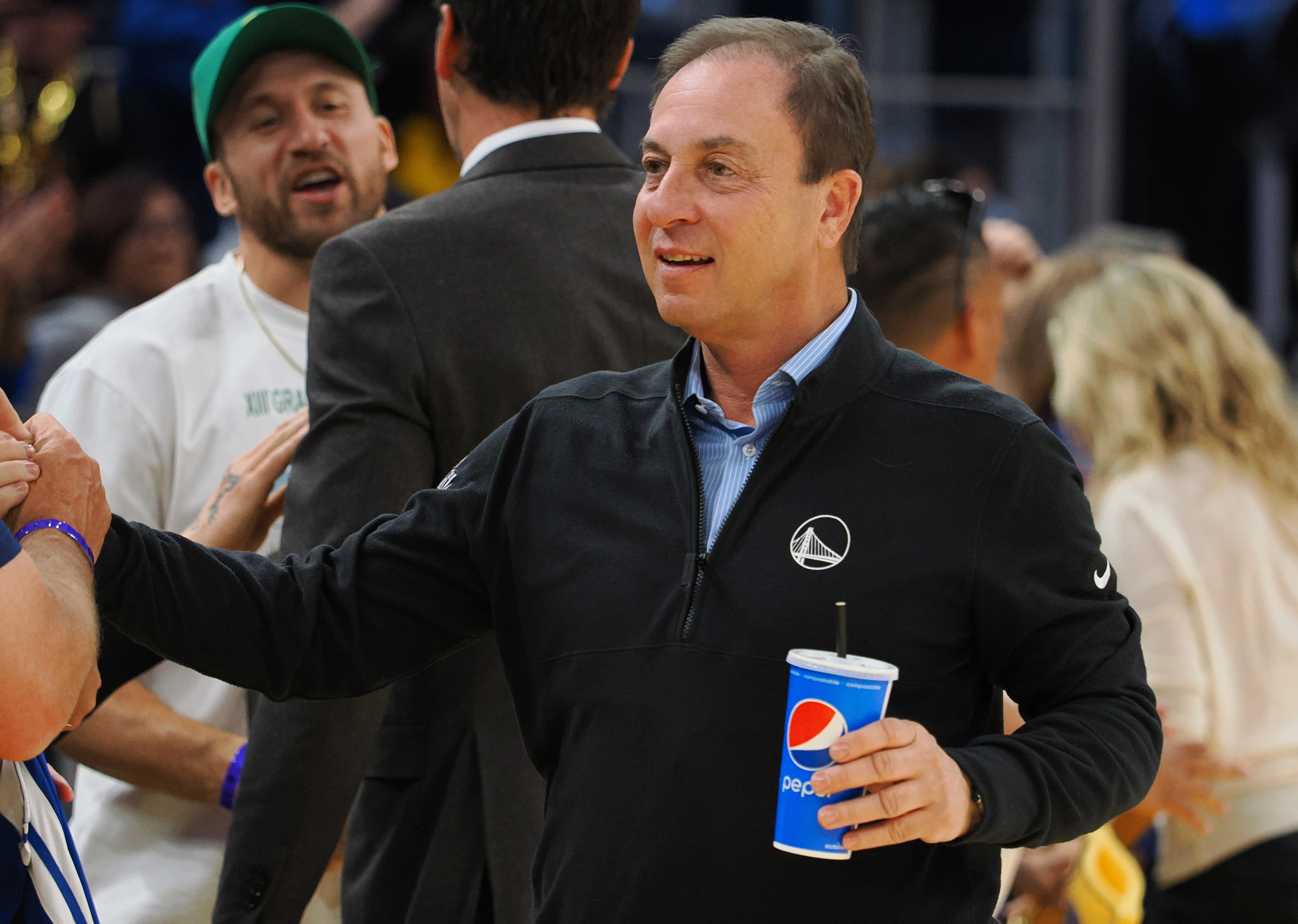 Joe Lacob smiling on the sidelines, holding a drink