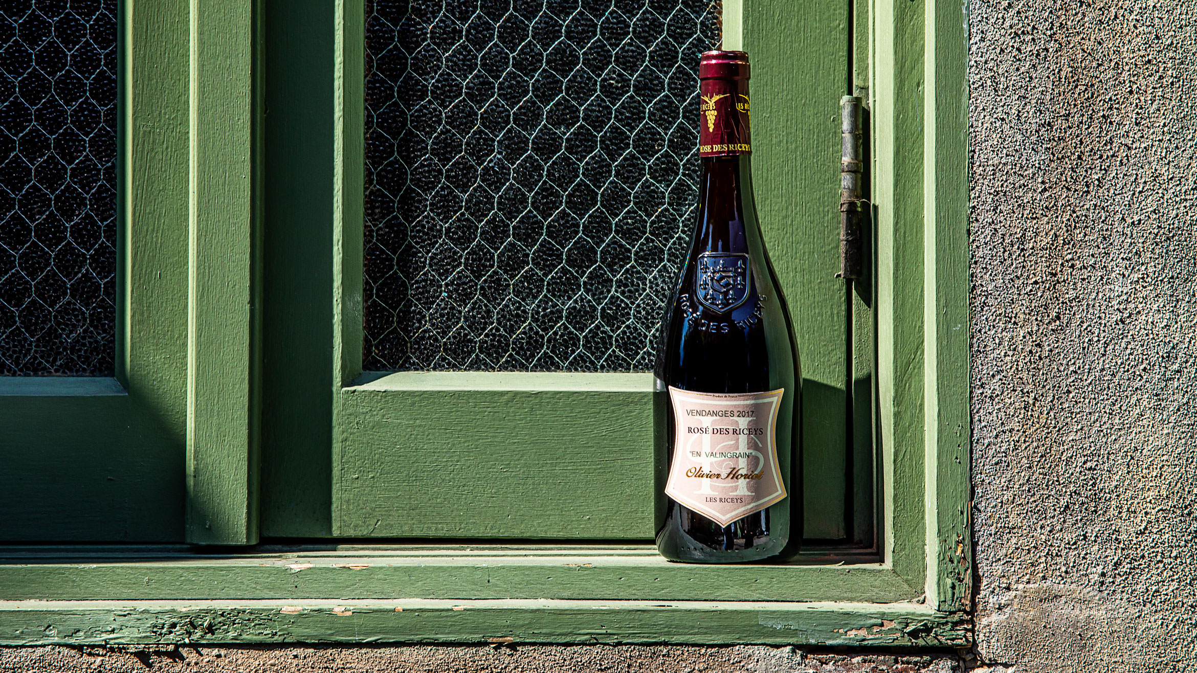 A bottle of wine sits in an exterior wooden windowsill.