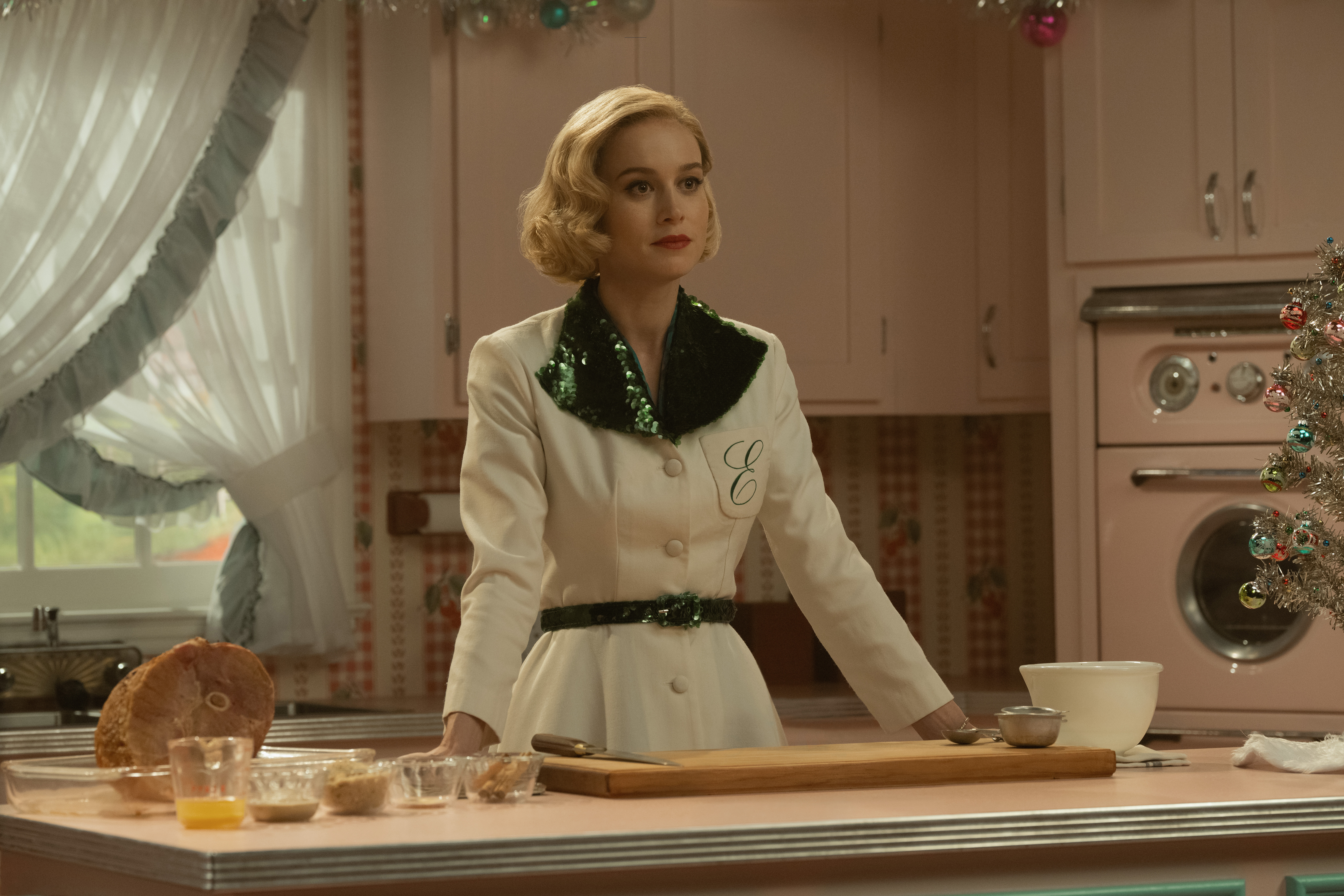 Actress Brie Larson, in a ‘50s-style housecoat, stands behind a kitchen counter. 