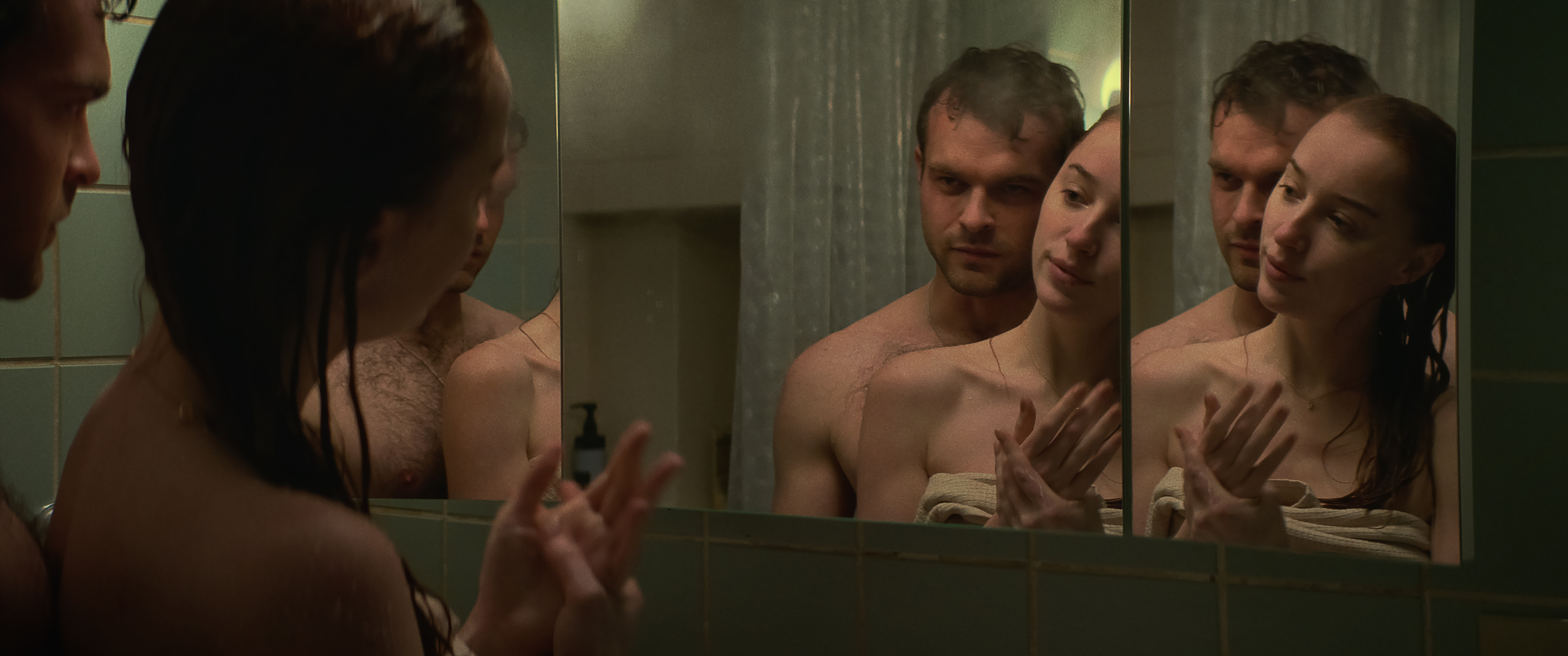 Luke (Alden Ehrenreich) and Emily (Phoebe Dynevor), both wet from the shower and with Emily only wearing a wrapped towel around her torso, look at multiple reflections of themselves in their bathroom mirrors in Netflix’s Fair Play
