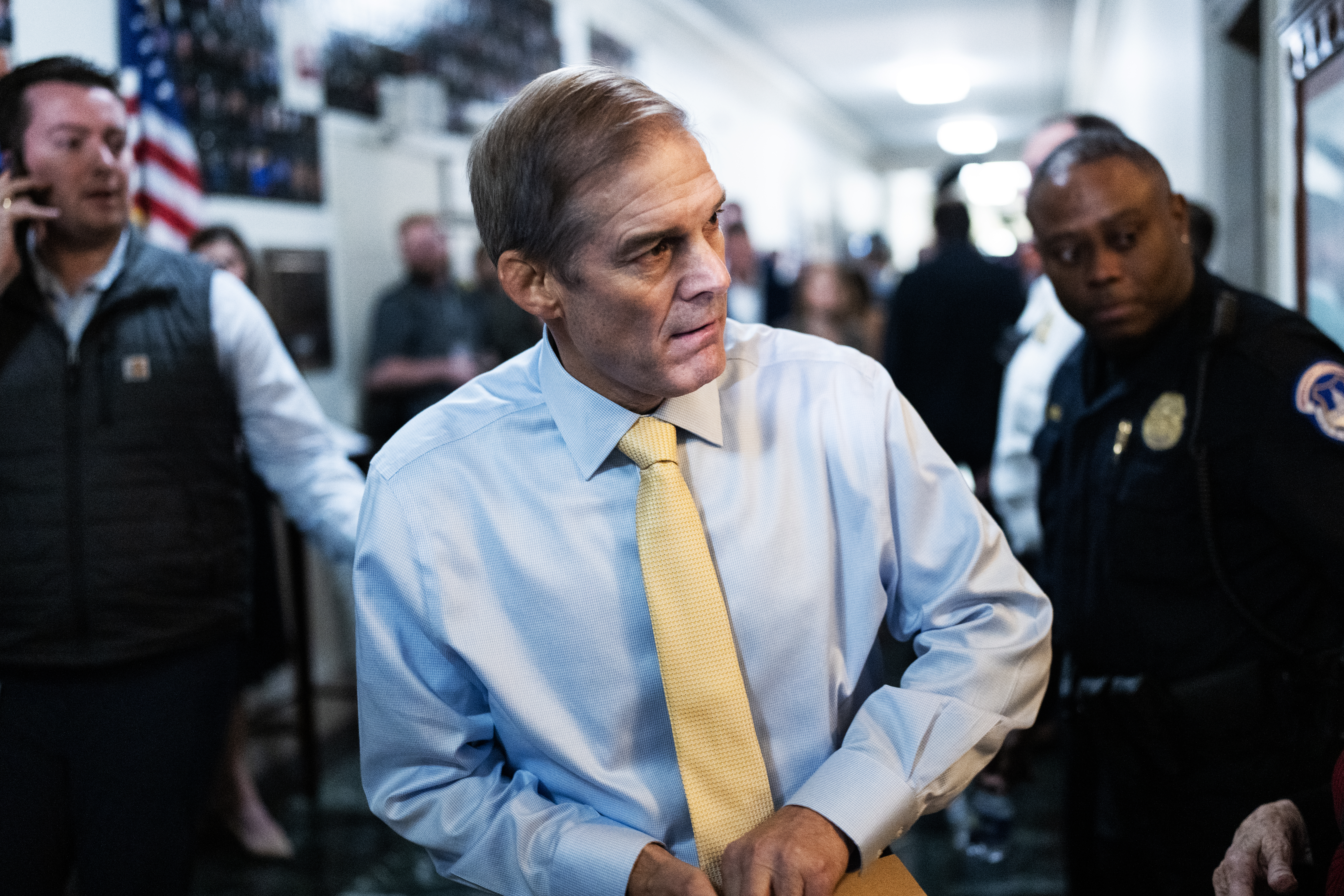 Jim Jordan wears a light blue dress shirt and light yellow tie. A security officer stands in the background.