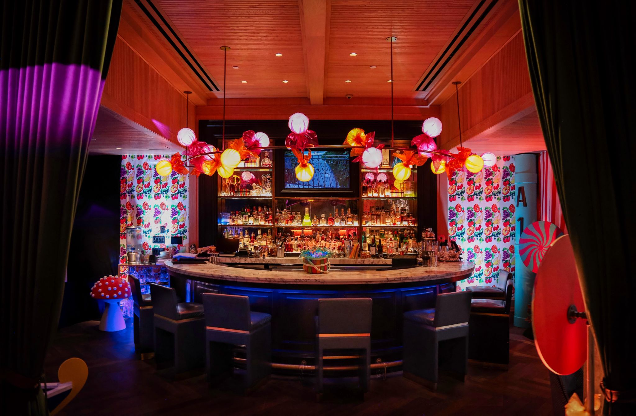A brightly colored bar bathed in red lights with lights wrapped in candy wrappers and mushroom toadstools. 