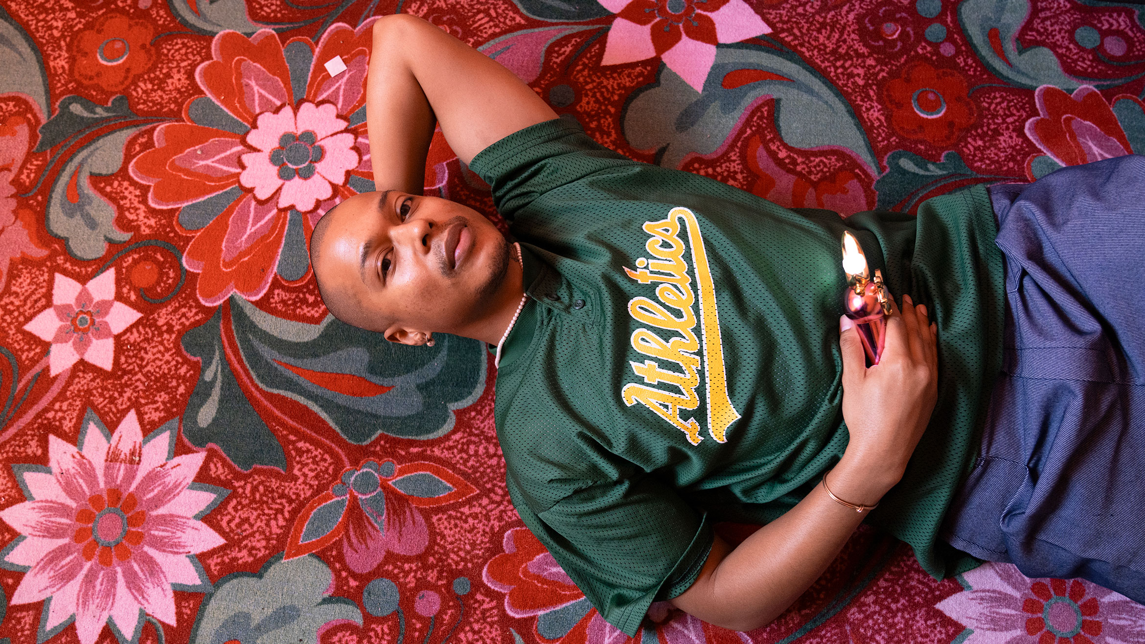 A person wearing an Athletics jersey lies on their back on a floral carpet.