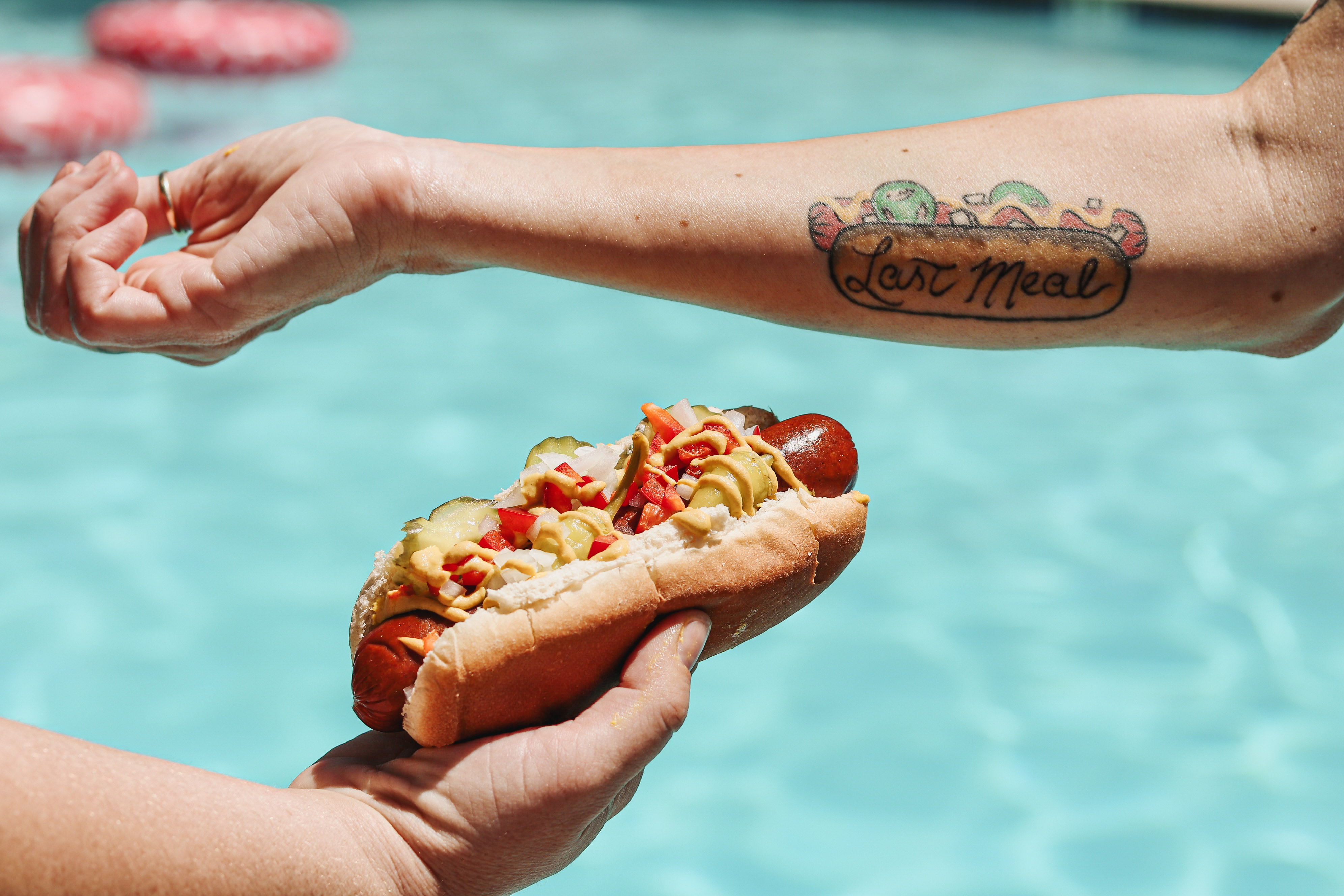 Someone holding up a hot dog next to another person’s arm tattoo