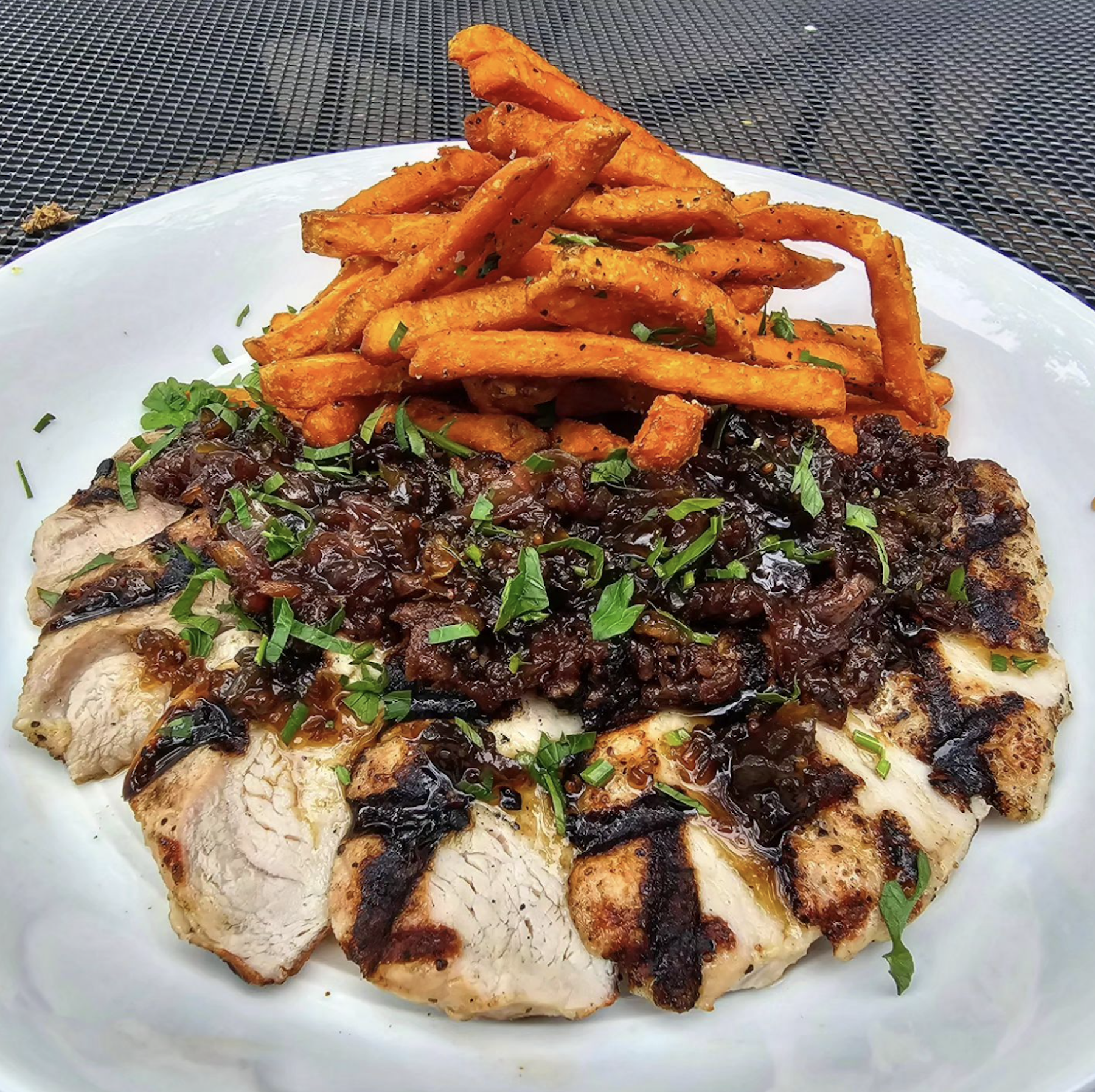 A dish of sliced pork, topped with a caramelized garnish and roasted sweet potato fries.  