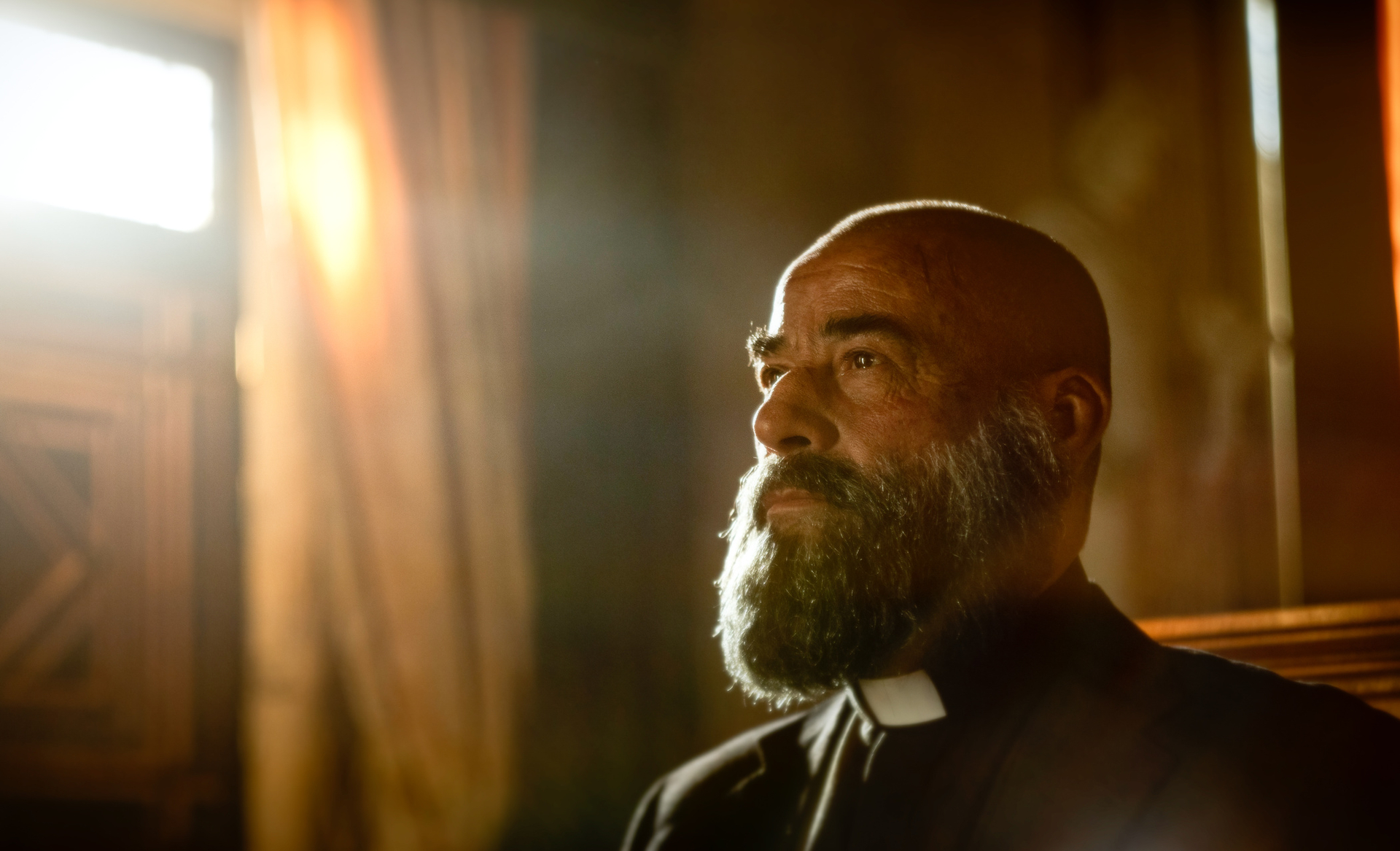 Father Vergara (Eduard Fernández) looking holy with a warm, glowing light coming in to the side of him