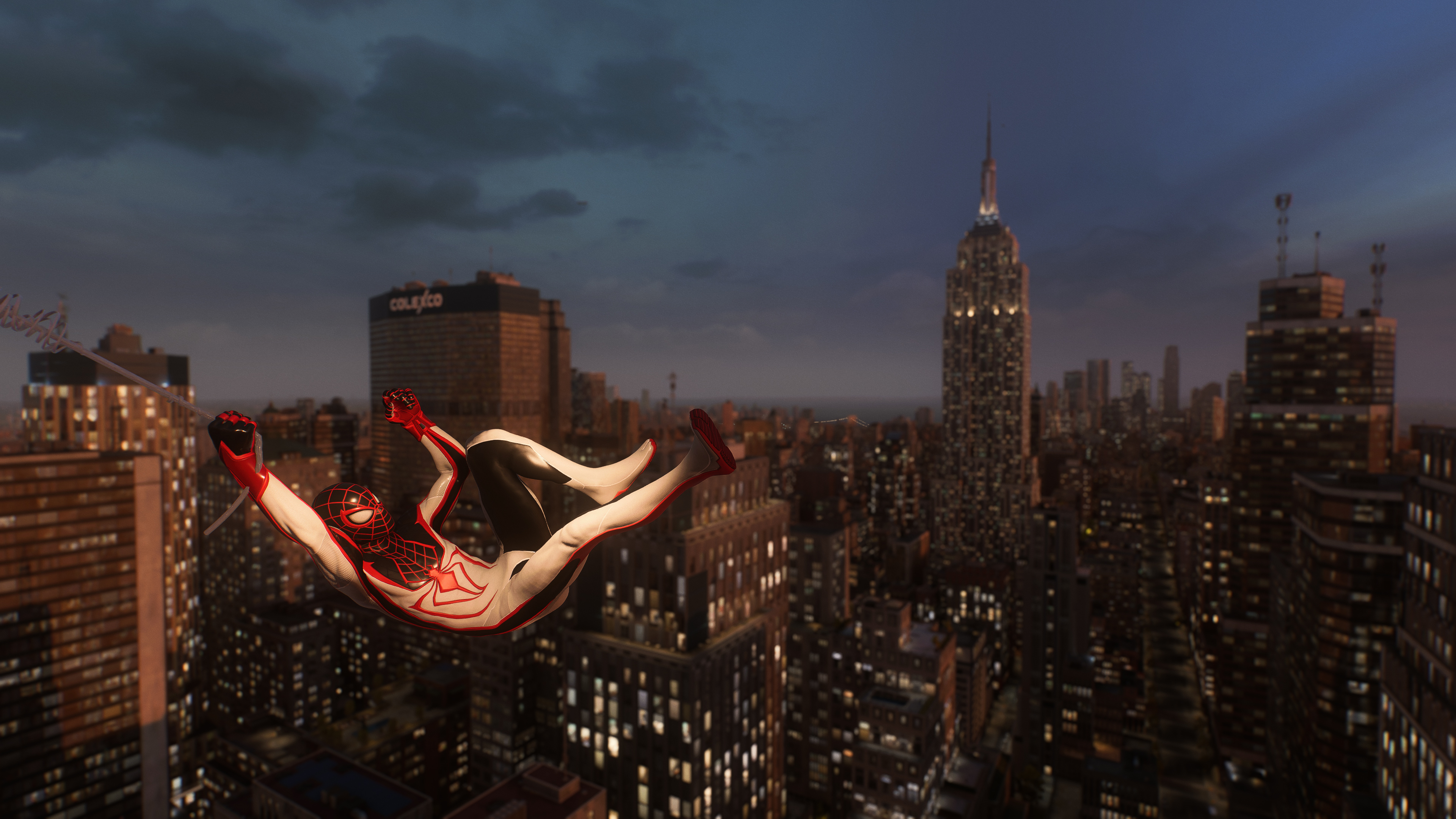 Miles Morales swings above Midtown Manhattan in Marvel’s Spider-Man 2 at dusk, while wearing the T.R.A.C.K. suit